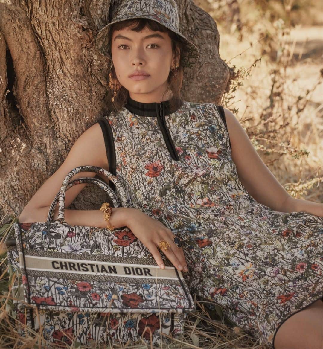 のインスタグラム：「Nestled amid the Puglian nature that inspired both it and the primary #DiorCruise 2021 collection by @MariaGraziaChiuri, the 'Mille Fleurs' motif created by @PietroRuffoArtist from the eponymous capsule unfurls across an updated embroidered #DiorBookTote with matching techno taffeta short-sleeved dress and reversible bucket hat. For more, tap the link in bio. © Photos: @SarahBlais」
