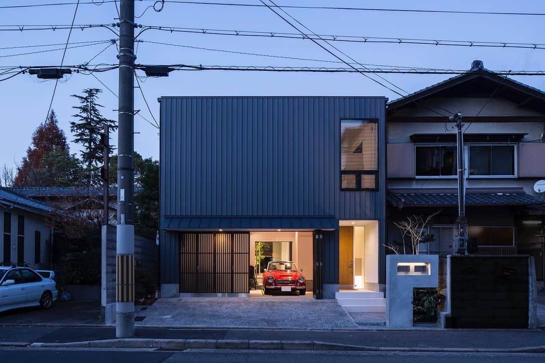 ザウス住宅プロデュースのインスタグラム：「…優しい灯りが漏れるガレージハウス：京都    •  黒のガルバリウム鋼板で覆われた外観に、木製の格子戸にアクリル板がはめられたガレージドアから、行燈のようにうっすらと光がもれ、建物を浮かび上がらせる視覚を感じれる設計  　　　 設計：田中幸実建築アトリエ 撮影：笹倉洋平   　　　 #garagehouse#garage#car #ダットサンフェアレディ#home#architecture#design#zaus #田中幸実 #笹倉洋平 #ザウス#ガレージハウス#建築#建築家との家づくり#暮らしを楽しむ」