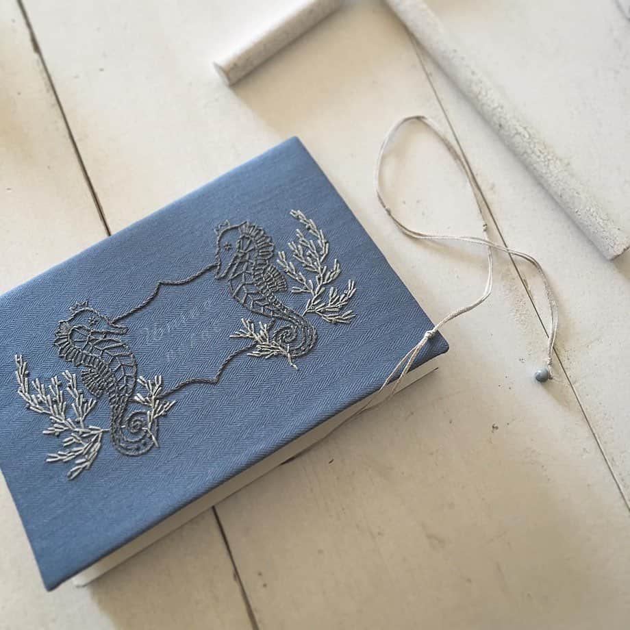 手紙社のインスタグラム：「【残しておきたい記録や日記、レシピ帳などに「刺繍入りノートブック」はいかが？】﻿ 自然の造形や愛する横浜の景色をモチーフに作品を制作する「yazawado」。布博で販売中の「刺繍入りノートブック」は、落ち着いたブルーの生地に向かい合うタツノオトシゴが刺繍されたノートブック。細いリネンの紐の先には小さなグレーのアンティークビーズを。くるくると巻きつけて、あなたの大切な一冊にしてみてくださいね。きっとタツノオトシゴたちが見守ってくれるはず。﻿ ﻿ ▶︎「yazawado（@yazawado）」さんのショップは「12/22（火）22:00」まで販売中！﻿ ﻿ ＜新しいオンラインフェスティバル・布博　開催概要＞﻿ 会期：2020年12月14日（月）〜26日（土）﻿ チケット：一般 1,000円／手紙社の部員 900円﻿ 会場：「新しいオンラインフェスティバル・布博」公式サイト﻿ ▶︎詳細は「@textilefabrics」プロフィールのURLから！﻿ ﻿ ーーーーー﻿ ﻿ ◎「新しいオンラインフェスティバル・布博」は3本立て！﻿ ﻿ 1）オンラインミーティング（番組）﻿ ▶︎12/14（月）〜19（土）毎日開催！﻿ 出展者による作品紹介やアトリエツアーなどの番組を生配信！﻿ 作り手との会話をお楽しみいただけます。﻿ ﻿ 2）オンラインショッピング﻿ ▶︎12/14（月）〜毎日異なる出展者が販売を開始します！﻿ 出展者による新作や、ここでしか買えない限定作品、もちろん、定番商品も購入することができます！﻿ ※それぞれの販売期間は公式サイトからご確認ください﻿ ﻿ 3）スペシャル音楽ライブ番組﻿ 12/20（日）は7時間を超える生放送をお届け！﻿ 豪華アーティスト4組による音楽ライブや、プロのスタイリストが布博アイテムのスタイリングを紹介する「ライブスタイリング」を生配信します！﻿ ﻿ #手紙社#手紙舎#布博#オンラインイベント#新しいオンラインフェスティバル#新しいオンラインフェスティバル布博#ブローチ博#布雑貨#手芸#テキスタイル#刺繍#ブローチ博#ハンドメイド#編み物#ノートブック#刺繍#yazawado#tegamisha#nunohaku#textile#textiledesign#fabric#handmade#handcraft#accessory#embroidery」