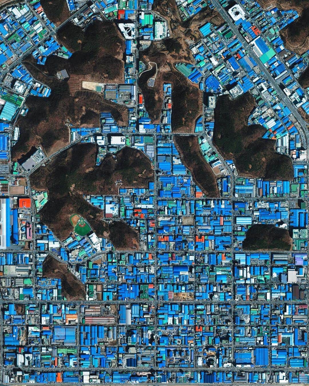 Daily Overviewのインスタグラム：「Choji-dong is a neighborhood of roughly 55,000 people in the city of Ansan, South Korea. The Korean government has intensively driven development of Ansan, particularly in this area, with an emphasis on manufacturing. The striking blue color shown here results from the use of aluminum roofing, which is used for its low cost and longevity. - Created by @overview Source imagery: @maxartechnologies」