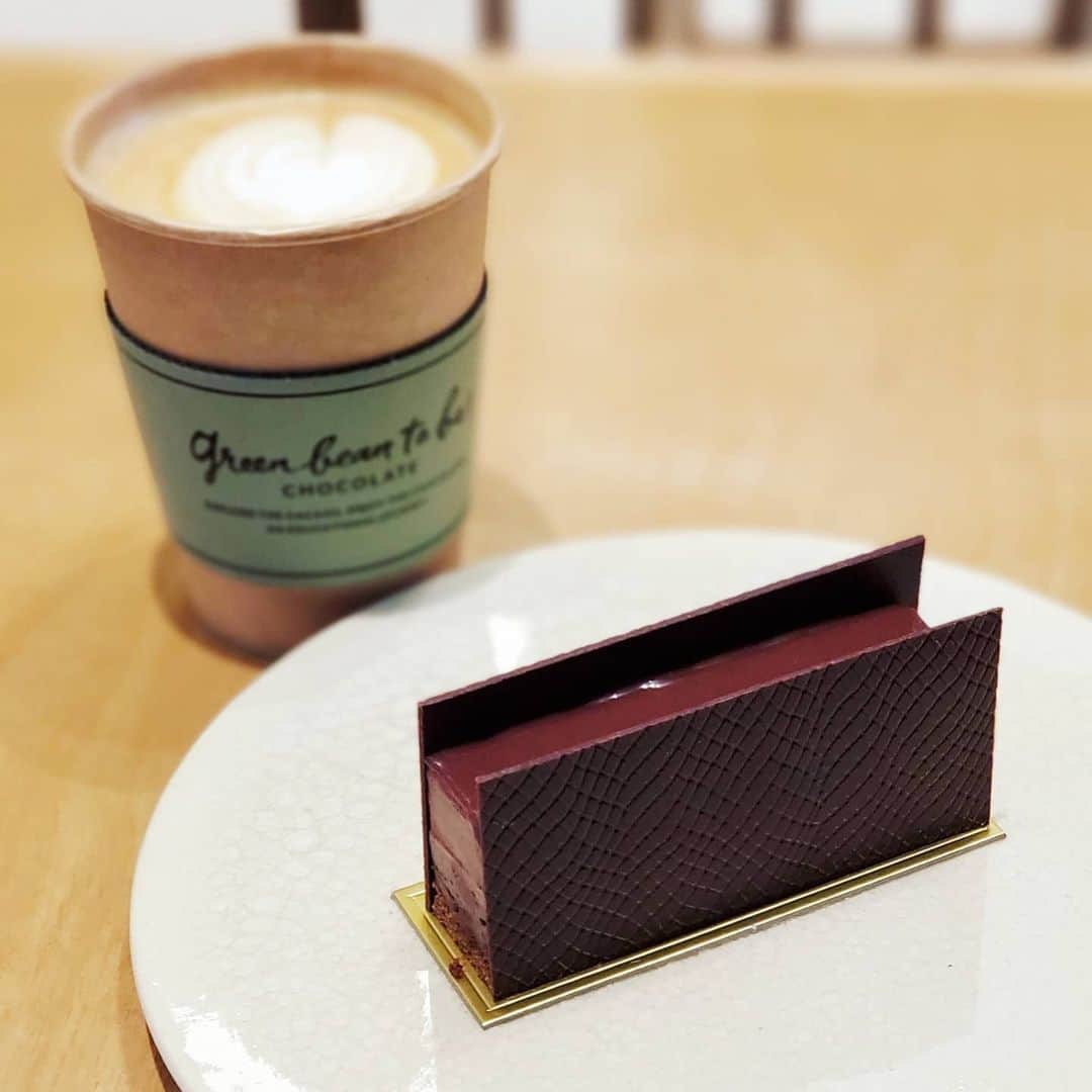 のインスタグラム：「ちょちょちょチョコレート♪ 【green bean to bar CHOCOLATE】 🍫マラノン ☕カフェラテ  日本発のBean to Bar chocolateメーカーのチョコレートショップ チョコレートバー、ボンボンショコラやガトーショコラなど購入できますが、カフェも併設していて各種チョコレートケーキやブラウニーなど楽しめます  ケーキでは、コロンとかわいいエクレアがインスタで人気ですが、黒猫チョイスは 日本ではココでしか味わえない“ペルーのマラノン・キャニオン”のカカオ豆を使った｢マラノン｣ チョコレート生地、ガナッシュ、ムース、そしてTOPのグラサージュと4層のチョコレートケーキ さらに両側にチョコレートバーを貼り付ける贅沢な一品に、テンションMAXひゃっほー！😺. . . 🚶東京都中央区日本橋室町3-2-1 コレド室町テラス1F 三越前駅から地下通路直結 営業日、営業時間などはお店のSNSを @greenbeantobar_chocolate  #黒猫食べ過ぎ #greenbeantobarchocolate #beantobar #コレド室町テラス」