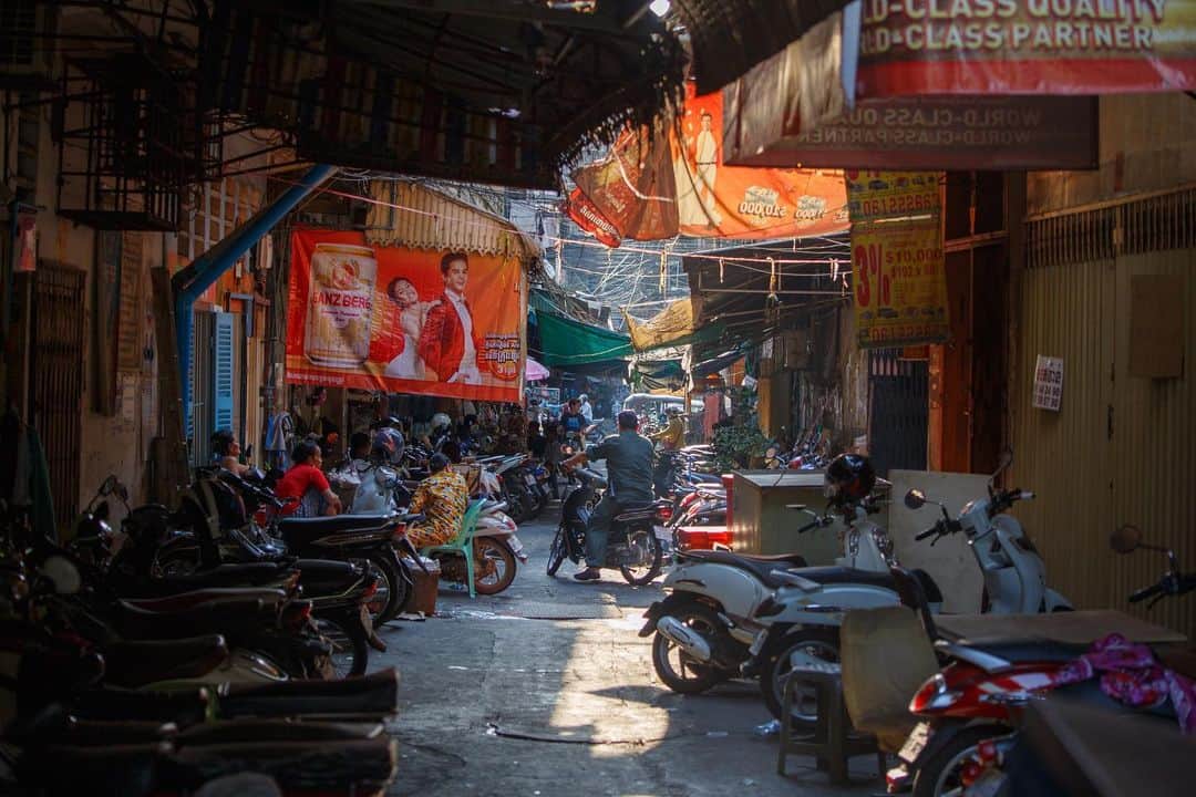 Shunsuke Miyatakeのインスタグラム：「A small talk at a back alley. “Where are you going?” the women asked a man. And a man answered “I'm going to pick up my daughter from elementary school” The light was coming through the gap of roof. 0417pm, Phnom Penh, Cambodia」