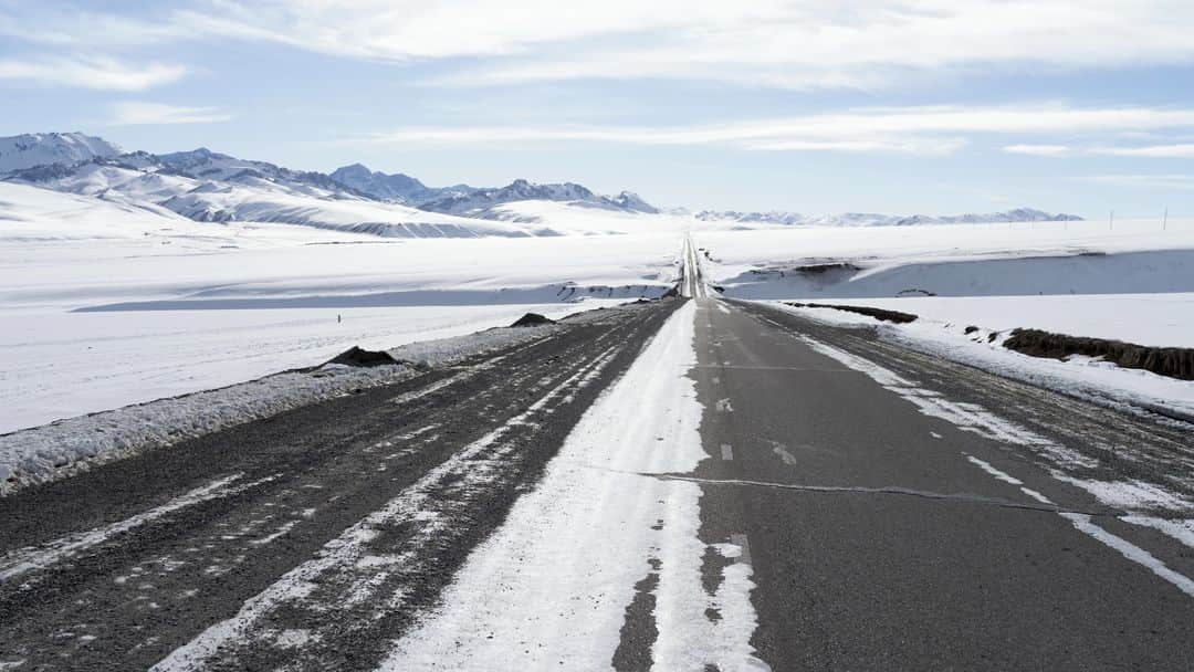 ルモンドのインスタグラム：「La route déroule son ruban d’asphalte à travers les steppes enneigées, entre l’épine dorsale du Tian Shan, chaîne de géants tutélaires drapés de blanc, et une rangée de collines de terre rouge ciselées par l’érosion. C’est là, sur le bas-côté, à 100 kilomètres du col de Torougart et de la frontière chinoise, et à 400 kilomètres de Bichkek, la capitale du Kirghizistan, sur un rectangle plat de deux kilomètres sur un, que devait s’ériger la « zone industrielle, commerciale et logistique sino-kirghize d’At-Bachy ».⁣ C’était compter sans la dizaine de milliers d’habitants d’At-Bachy, le chef-lieu de district, situé à cinquante kilomètres à l’est. Ils vivent du petit commerce et, surtout, de l’élevage.⁣ « Ici, il n’y a pas assez de travailleurs spécialisés. Alors d’où viendraient-ils, ces milliers d’employés ? De Chine, pour moitié d’entre eux ! Et les Kirghiz n’auraient eu que des postes subalternes, le gardiennage. La zone est en amont des villages, à l’ouest, d’où viennent le vent et la rivière : ça nous aurait pollués. Nos ressources sont bien trop limitées », résume Junusaliev Mederbek, 57 ans, réparateur en électronique, dans son gros anorak, chapka sur la tête, dans la petite pièce chauffée d’un restaurant d’At-Bachy où une matrone sert le thé.⁣ -⁣ 1-9 : La route principale menant d’Al-Bachi, au Kirghizistan, au col de Torougart, à la frontière chinoise, le 12 janvier 2021⁣ 2 : De l’ex-future base industrielle chinoise ne restent plus qu’une station-service et un motel pour routiers⁣ 3 : Junusaliev Mederbek (à gauche) est l’un des meneurs de la contestation contre le projet de zone industrielle chinoise à At-Bachy. Il lit un poème à Guljan Aitbaeva, dans un restaurant de la ville, le 13 janvier, pour la remercier de son soutien⁣ 4 : Des chasseurs ont capturé des loups ayant attaqué le bétail d’un village reculé⁣ 5-6 : À Bichkek le 10 janvier, le bazar Madina est construit en containers empilés⁣ 7 : Un panneau vantant les « nouvelles routes de la soie » chinoises⁣ 8 : Deux fillettes observent leur père réparer sa voiture devant le motel pour routiers d’At-Bachy⁣ -⁣ Photos : Yam G-Jun (@yamgjun) #PourLeMonde⁣ -⁣ #Kirghizistan #routedelasoie #economie」