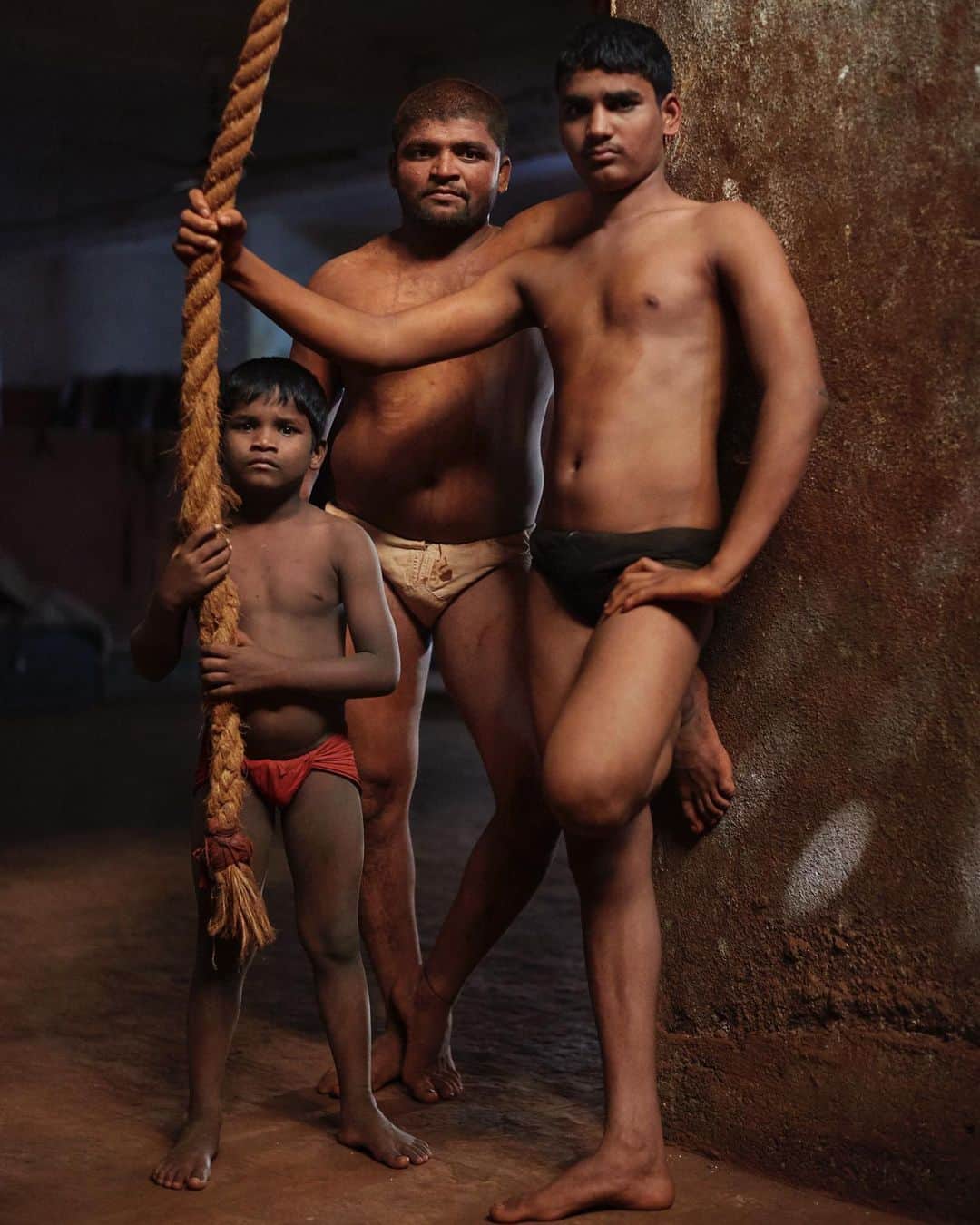 スコット・シューマンのインスタグラム：「When I was visiting Pune a few years ago I heard about a wrestling club that helped young men in need.  I stopped by and because the way natural light filtered in through small, high placed windows the place looked like a movie set!  I was actually photographing someone else when I glanced behind me and saw these three young men watching me while standing in just the exact positions you see them in this image.  Wrestling Club Pune, India 2017」