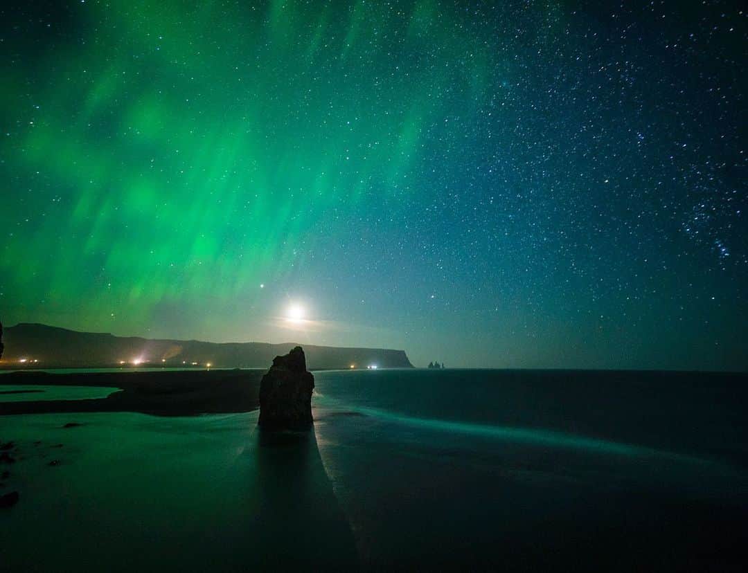 クリス・バーカードのインスタグラム：「Moon rising over Arnardrangur. This has always been one of my favorite photographs, It truly felt like a right place at the right time scenario. Northern lights coming out of the East while the stars light up over the ocean. You can even see Orion’s belt on the right of frame. But it’s the shadow of the moon being cast around the sea stack Arnardrangur that feels almost ghostly in this photograph. These details can be hard to articulate but also important when deciphering what to look for in a landscape.」