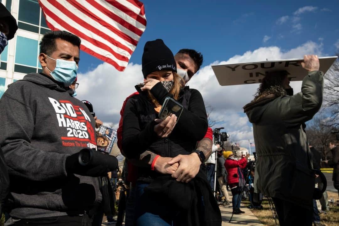 のインスタグラム：「Photo by David Guttenfelder @dguttenfelder / Rubia Garcia of New Orleans wipes a tear as she and Nick Larsen of Kenosha, Wisconsin, watch the Inauguration on their phone as they gather with a crowd outside the Capitol Building. They stood beside Javier Lugo (left), who came with his son Javier Antonio Lugo, and Jack Burns (right), who carried a sign directed at Trump supporters that read: "You're in a cult."」