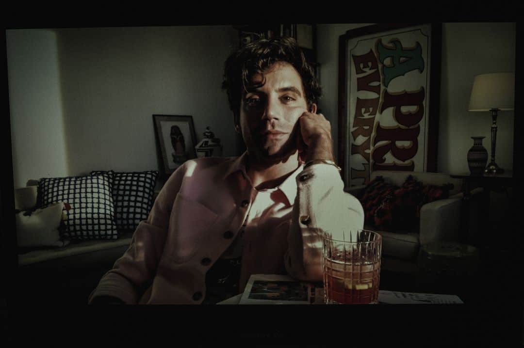 ルモンドのインスタグラム：「On s’attendait à voir le chanteur Mika surgir sur l’écran tel un zébulon, vêtu d’une de ces invraisemblables tenues patchwork acidulées qui ont fait sa marque de fabrique. On imaginait un intérieur pop, entre « L’Ile aux enfants » et Andy Warhol. On le pensait à Miami, où il possède une maison, en Toscane, où il se réfugie une partie de l’année, ou à Paris, puisqu’il vient d’enregistrer un show au château de Versailles, diffusé le 5 février sur France 5. On le trouve à Athènes, dans un immeuble déglingué des années 1970. Il apparaît dans un tee-shirt noir sur pantalon blanc et nous fait visiter avec son portable le studio où il écrit, un capharnaüm où s’entassent cartons à même le sol et piles de livres sur des étagères bon marché.⁣ Son confinement grec de trois mois et demi, il raconte l’avoir mis à profit pour étudier la philosophie et les relations internationales, et pour apprendre l’arabe. Quatre heures de cours par Zoom en plus des devoirs imposés par ses profs à distance, de l’écriture de son sixième album et de la confection de petits plats. « Un soir, alors que je sortais quelque chose du four, j’ai entendu un morceau de musique qui m’a fait pleurer. C’était comme une décompression du cerveau, ça ne m’était pas arrivé depuis longtemps. C’est la première fois de ma vie que je me posais, je suis redevenu quelqu’un qui écoute de la musique et plus seulement un interprète. Cette pandémie m’a paradoxalement reconnecté avec le monde. Plus j’étais enfermé à la maison, plus j’étais curieux de l’extérieur. »⁣ -⁣ Mika chez lui, à Athènes (Grèce), le 4 février 2021, photographié à distance par Zoom. Photo : Frédéric Stucin (@fredstucin) / Pasco (@pascoandco) #PourLeMonde⁣ -⁣ #apero #musique #culture」