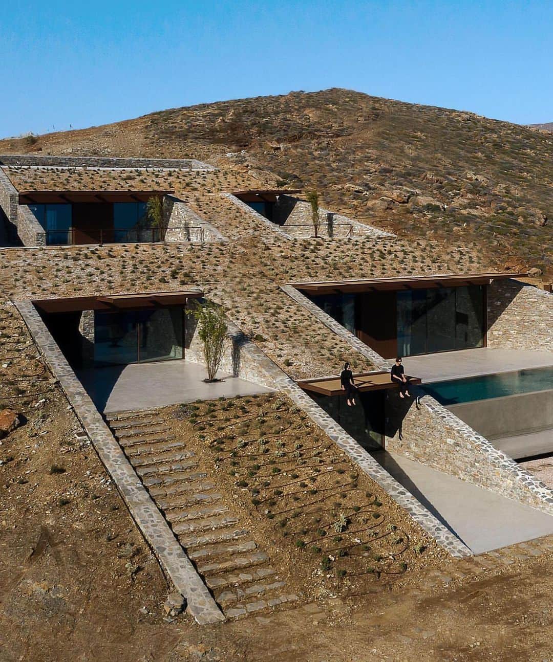 The Cool Hunterのインスタグラム：「Designed by Athens-based @moldarchitects nCAVED is currently high on our list of genuinely original yet refreshingly unpretentious vacation residences. The drama of the severe rocky landscape is repeated with dramatic skill in the chiselled strictness of the building.  Completed in 2020, nCAVED’s 340 square metres (3,660 sq.ft) of space disappear into the rock in a protected cove on the island of Serifos. From the outside it brings to mind the entrance of a pyramid or tomb. Yet from the inside, the living rooms are filled with natural light and afford spectacular views of the Aegean Sea. The strong northerly winds of the sea were one of the key considerations in the planning process that resulted in a dramatic solution providing both extreme shelter and stunning views. (Link in profile) #swipeleft」