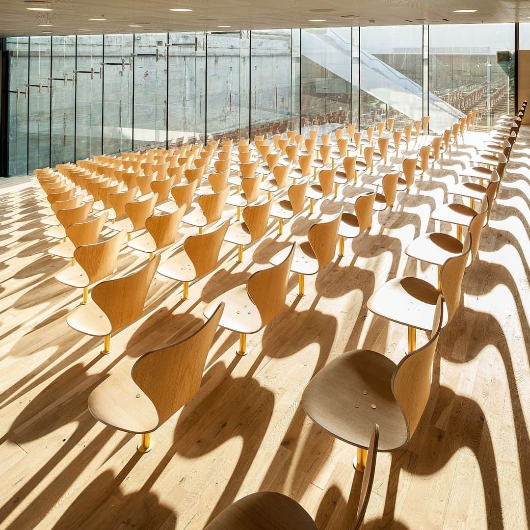 のインスタグラム：「The Danish Maritime Museum is located north of Copenhagen next to Kronborg, the castle that inspired Shakespeare's writing of Hamlet.   This photo of the auditorium reveals its impressive modern architecture and a glorious play of light and shadow between  Series 7™ seating.   A sea of Series 7™ chairs in oak emerge from the oak floor, mounted on gold plated columns. The surrounding dock is raw concrete.  Architecture by @big_builds   Read more about this space via link in bio」