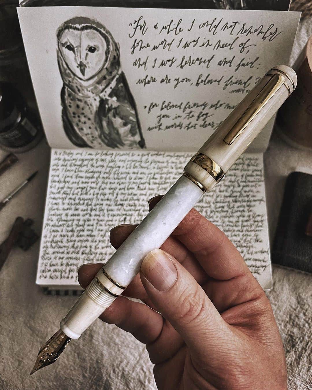 Catharine Mi-Sookさんのインスタグラム写真 - (Catharine Mi-SookInstagram)「Continuing in my study of owls. I’m fascinated with the barn owl and keep coming back to her. Today I dusted off a palette of black paints for a change and it helped me learn more about depth and texture in a new way. A dip-penned quote by Mary Oliver to accompany, inspired by the sweetness of friendship, which reminded me that when the fog descends as it inevitably does along the terrain, sometimes it is the words of a friend who help clear the way. I am grateful for this reminder today and always. . . . . Leather Tome Journal, Mini Journal & Antique Textile Pouches @pegandawl. Winter 325 Fountain Pen @labanpen. 1901 Pencil & Sterling Silver Extender @franklinchristoph. Watercolors @greenleafblue. Candles @natureskindle. . . . . #artjournal #barnowl #owlpainting #memoirs #pegandawl #bookbinding #leatherjournal #handmadebook #labanpen #fountainpen #penmanship #franklinchristoph #graphiteart #greenleafblueberry #watercolorsketch #artjournalpages #booksandcandles #ofsimplethings #poetryofsimplethings #lightacademia #alittlebeautyeveryday #myquietbeauty #beautyofstillmoments #watercolorpractice #nestandflourish #thesweetlifeunscripted #inspireddaily」1月30日 3時18分 - catharinemisook