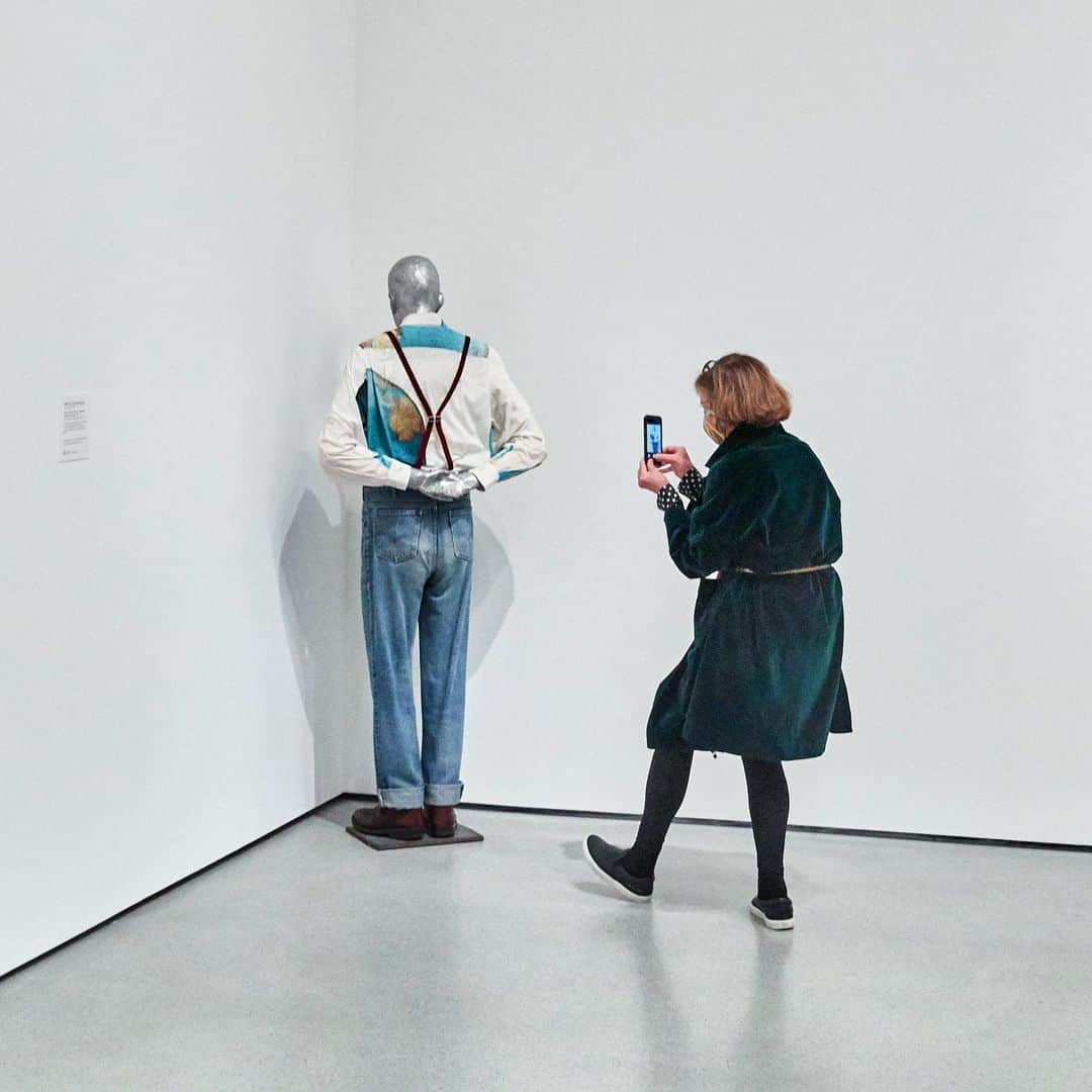 ニューヨーク近代美術館のインスタグラム：「There's something new to discover in every corner of our collection galleries 👀   #MartinKippenberger's full-scale replica of himself is posed like a naughty schoolboy doing his penance in the corner of our second-floor gallery, After the Wall, featuring works by European artists made in the wake of political and social revolutions of the late 1980s.  The German artist was known for his outrageous and provocative behavior, both in his art and his personal life. Spurred by a particularly vicious article by a German art critic, Kippenberger created six "Martin in the Corner" sculptures.  While the other figures are dressed more formally, this one, commissioned by MoMA, wears Levi's jeans and a shirt with a globe on it, a nod to casual American fashion and the Museum's role as an international center of modern art.  Explore the gallery—and plan your next visit—at the link in our bio. — [Martin Kippenberger. "Martin, Into the Corner, You Should Be Ashamed of Yourself." 1992. Cast aluminum, clothing, and iron plate. © 2021 Estate Martin Kippenberger, Galerie Gisela Capitain, Cologne. Photo by Gus Powell] #MoMACollection」