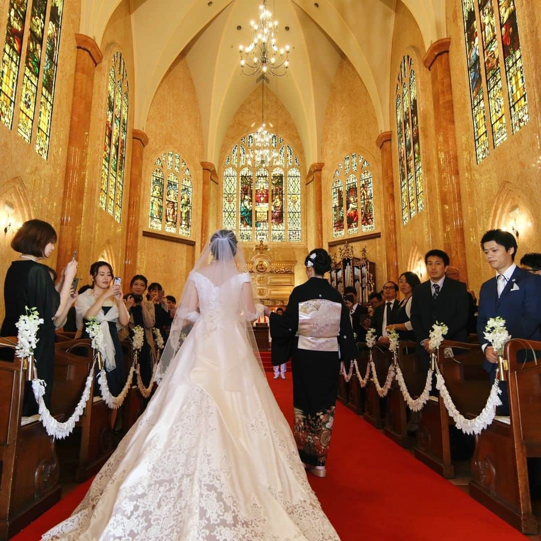 マリエカリヨン名古屋のインスタグラム：「@marieecarillon . ステンドグラスから差し込む光に 導かれていく花嫁さまとお母さま。  神聖な空気の中、バージンロードを歩む時間は、 美しくかけがえのない思い出に... . ▼ブライダルフェアは インスタのTOPからご予約が出来ます⚐ ＞＞＞ @marieecarillon . マリエカリヨン名古屋では、 お客様の安心安全を考慮して、 業界のガイドラインに沿って、 感染症対策を行ったうえで、 営業を行っております。 オンラインでのご相談も受け付けておりますので、 お気軽にお問合せ下さい。 . ------------------ . @marieecarillonをフォローして #マリエカリヨン #マリエカリヨン名古屋 のハッシュタグをつけて お写真を投稿してみてくださいね✳︎ . こちらの公式IG（@marieecarillon） で取り上げさせていただきます♡ . #式場見学 #プレ花嫁 #結婚式場 #名古屋結婚式 #結婚式  #ウェディングドレス #カラードレス #挙式　#挙式レポ #結婚式レポ #チャペル #大聖堂 #卒花嫁 #式場迷子 #披露宴 #結婚式準備 #日本中の花嫁さんと繋がりたい #東海プレ花嫁 #名古屋花嫁 #プレ花嫁準備 #入籍 #ステンドグラス #大聖堂 #トレーン #チャペルウェディング #バージンロード  #ベールダウン」