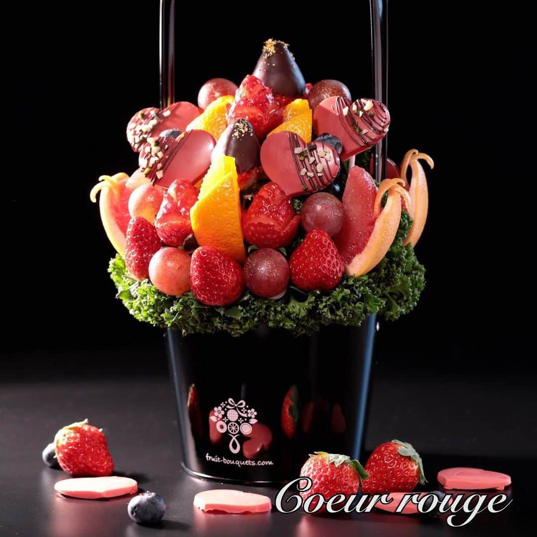 Fruit-bouquets.comのインスタグラム：「【バレンタイン期間限定】 Coeur rouge(クールルージュ) . 2021年の新作フルーツブーケ 💐 . クール ルージュはフランス語で 「赤いハート」💝🇫🇷 . 名前の通りシックな色合いの中に 情熱的な赤いハートをあしらった新商品✨ . 今年はスペシャルプライスにて お届けいたします💐 . 素敵なバレンタインをお過ごしください💖 . 人気のイチゴ、爽やかなオレンジと一緒に バレンタインには欠かせないチョコレートをアレンジメントし、 限定商品として販売いたします✨ . フルーツはその他にも ブドウやグレープフルーツ、 ブルーベリーも使用しています . チョコレートはすべて、一流パティシエも愛用する フランスのヴァローナ社のものを使用しています🍫 . 赤いハート型のチョコは、 ストロベリーフレーバーのチョコレートでお作りしており、 濃厚な薫りと甘さがお楽しみいただけます🍓 . #フルーツブーケ #プレジール #フルーツ #果物大好き #フルーツ大好き #スイーツ #お祝い #プレゼント #贈り物 #記念日 #フルーツパフェ  #フルーツギフト #フルーツケーキ #インスタ映え  #インスタ映えスイーツ #インスタ映えケーキ #花束  #フォトジェニック #パーティー #サプライズ  #サプライズプレゼント #いちご #いちごケーキ  #おうち時間 #ホームパーティー  #バレンタイン #バレンタインデー  #バレンタインチョコ #チョコレート」