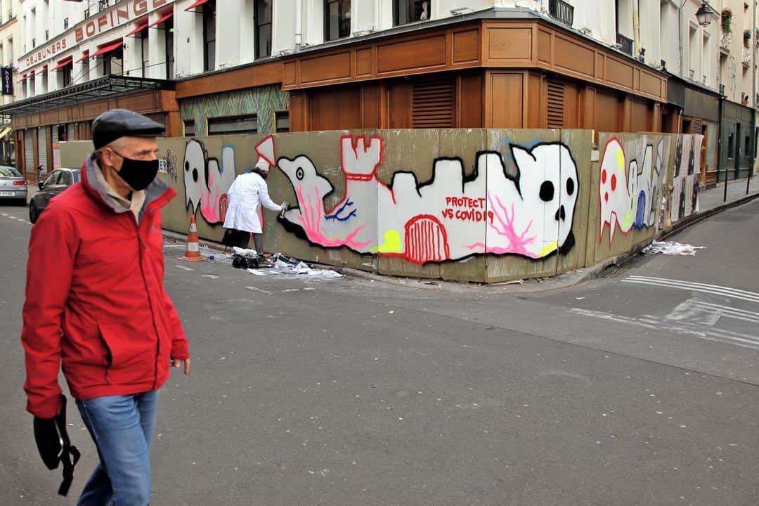 ルモンドのインスタグラム：「Samedi 2 janvier, 10 h 30, près de la place de la Bastille, à Paris, MGLO se dirige vers une palissade en bois qui protège les devantures de la célèbre brasserie Bofinger. Le street-artiste n’est pas au mieux, il craint d’avoir attrapé le Covid-19. A peine a-t-il entreposé ses pots de peinture sur les lieux qu’il part faire un test antigénique. Il revient quelques minutes plus tard rassuré. Il enfile une blouse pour mieux passer inaperçu, trempe son rouleau dans le pot de peinture blanche et se met au travail.⁣ Pour MGLO comme pour beaucoup de street-artistes parisiens la pandémie actuelle est devenue source d’inspiration, même si les restrictions ont quelque peu entravé le rythme de création.⁣ C’est le « Nous sommes en guerre ! », répété six fois par le président, le 16 mars 2020, qui a frappé Seth, un autre artiste parisien. « On doit tous porter des masques pour faire la guerre contre l’épidémie ? J’ai eu envie de peindre des enfants portant des heaumes », explique l’artiste.⁣ Madame, quant à elle, déployait, en décembre, deux immenses affiches portant sur l’impossibilité d’étreindre. « Si étreindre est au passé, aimer sera toujours imparfait », scandait la première, collée rue de l’Evangile (Paris 18e).⁣ Dans une veine plus mortifère, Retro est descendu, au lendemain du déconfinement, peindre dans la rue des squelettes colorés dansants. « J’avais l’impression qu’on voulait nous laisser sur la paille, tous nos projets en tant qu’artistes avaient été annulés. Je me suis dit : quand il ne reste plus grand-chose à part la couleur et l’énergie pour se motiver, alors faisons danser les morts »⁣ -⁣ 1 : Le graffeur MGLO (@mgloolgm) en train de peindre, le 2 janvier 2021, rue de la Bastille (Paris 4e). Photo : Thomas Von Wittich (@thomasvonwittich)⁣ 2 : Enfants aux heaumes de Seth dans les rues de la Butte-aux-Cailles (Paris 13e). Photo : SETH (@seth_globepainter)⁣ 3 : Madame (@madamedepapier), le 10 décembre 2020, rue de l’Evangile (Paris 18e). Photo : Thomas Von Wittich⁣ 4 : Retro (@retrograffitism), le 29 mai 2020, boulevard de Charonne (Paris 11e). Photo : Thomas Von Wittich⁣ -⁣ #streetart #art #covid」