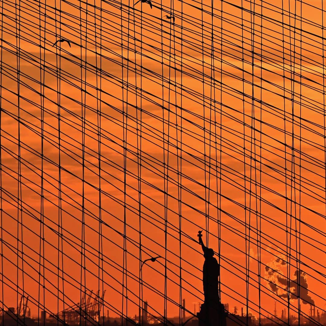のインスタグラム：「AFP Photo 📷 @angelaweissphoto - The Statue of Liberty is seen at sunset through the steel-wire suspension cables of the Brooklyn Bridge on February 17, 2021 in New York City.」