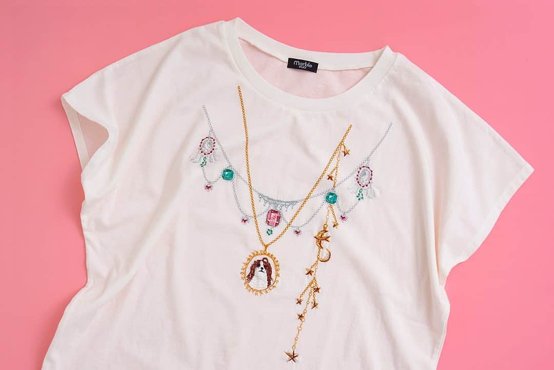 marbleSUD(マーブルシュッド) のインスタグラム：「今季の刺繍Tシャツはアクセサリー要らず⁉︎ 光り輝く豪華な宝石のネックレスがモチーフに。ペンダントトップには、前髪をちょこんと結んでおめかしした“シーズー”の姿が。  エメラルドやルビー、細いチェーンなど、繊細な刺繍で表現されたネックレスは今にも揺れだしそう。カーディガンを羽織ってもモチーフがしっかりと見えるのが嬉しいですね。」