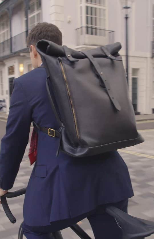 ジョンチャップマンのインスタグラム：「Which to choose - classy briefcase or cycle-safe backpack?  Chapman says both.   Our roll-top backpack with briefcase handle is the apogee of smart black leather discretion, ideal for the boardroom. And yet, as you cycle home in the evening, its clever perforated leather over reflective material will reflect car headlights. Brilliance shows.  Handmade in Carlisle since 1984.  #ChapmanMade #backpack #slowfashion」