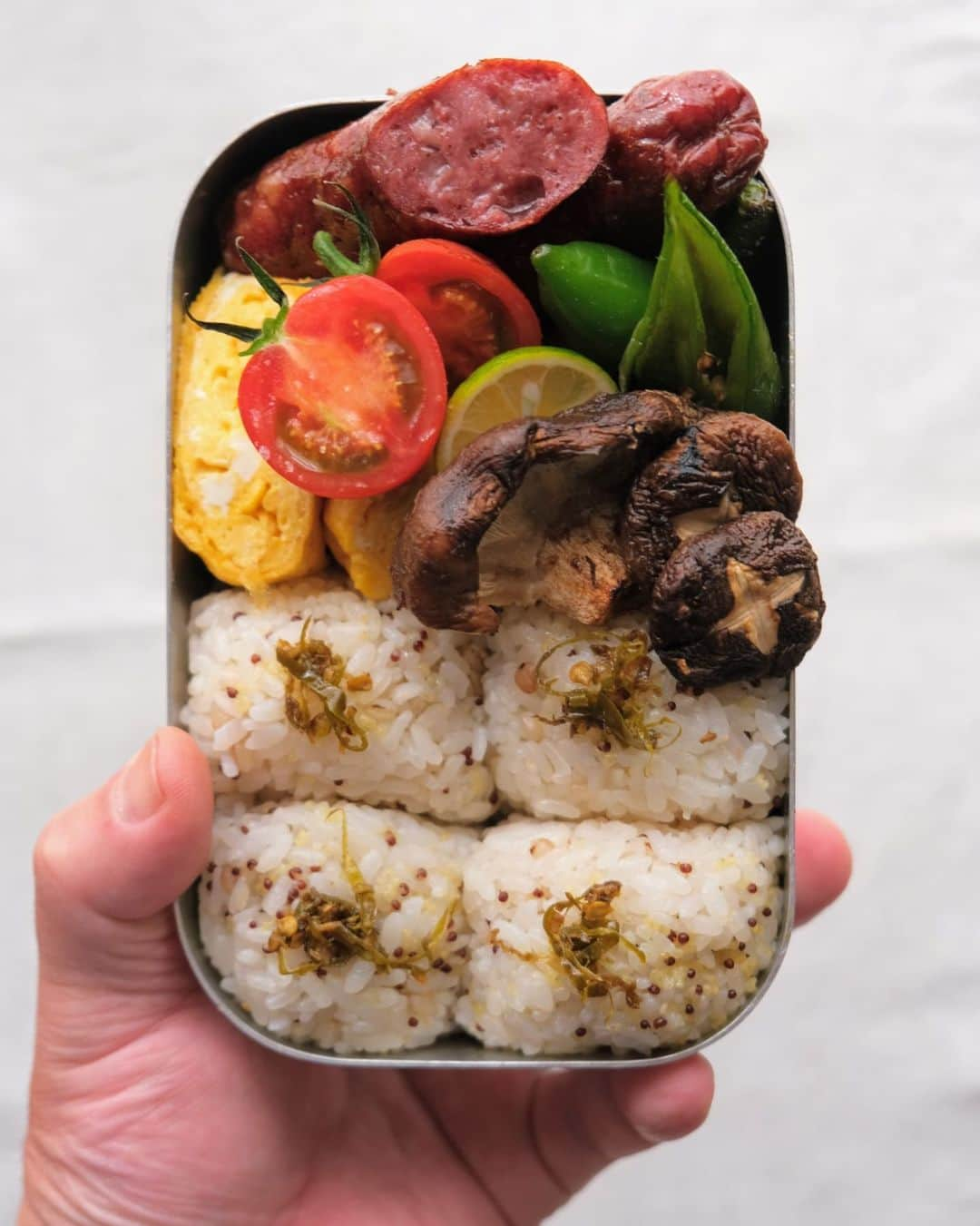 わたをのインスタグラム：「お昼だー🙌 今日は「にし阿波」の食材お弁当。  みまから添え雑穀米おにぎり。鹿肉のソーセージ。万願寺とうがらし焼きびたし。焼きしいたけ2種食べ比べ。トマト。  にし阿波とは 徳島県西部の美馬市、三好市、つるぎ町、東みよし町の2市2町からなる地域のこと。 広大な自然と伝統農法に支えられた、地域独自の県産品や食文化を持つ「食と農の景勝地」なのです。  徳島県人として、「にし阿波」の発信発展に協力させて頂きまーす🕺  ※訂正 画像3枚目にある「万年寺とうがらし」、正しくは「万願寺とうがらし」です🙇🏻‍♂️  #徳島 #にし阿波 #にし阿波スタイル #美馬市 #三好市 #つるぎ町 #東みよし町 #わた弁 #弁当 #お弁当 #弁当男子 #bento #Yummy #delicious #Japan #Japanesefood #Japaneselunch #bentobox #lunchbox #onigiriaction」