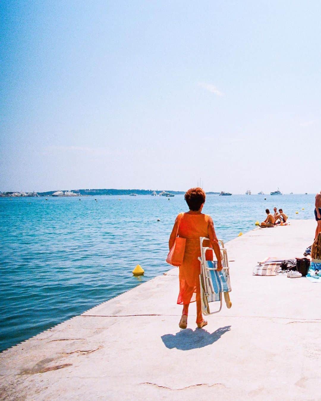 Pete Halvorsenさんのインスタグラム写真 - (Pete HalvorsenInstagram)「“Dame en Orange”  The lady in orange. While wandering along Boulevard de la Croisette a woman in an orange dress and matching handbag making her way out towards the sea caught my eye. She looked to have stepped out of the 1960s and into 2018. I watched her reach her destination, a small cement jetty where two groups of teenagers were enjoying the sun. There it was a classic Cannes backdrop with cruise ships and blue waters of the French Riviera. I composed the frame...A single moment captured on my Leica, the light frozen in time on Kodak Film...and now minted on the blockchain.」3月7日 2時02分 - petehalvorsen