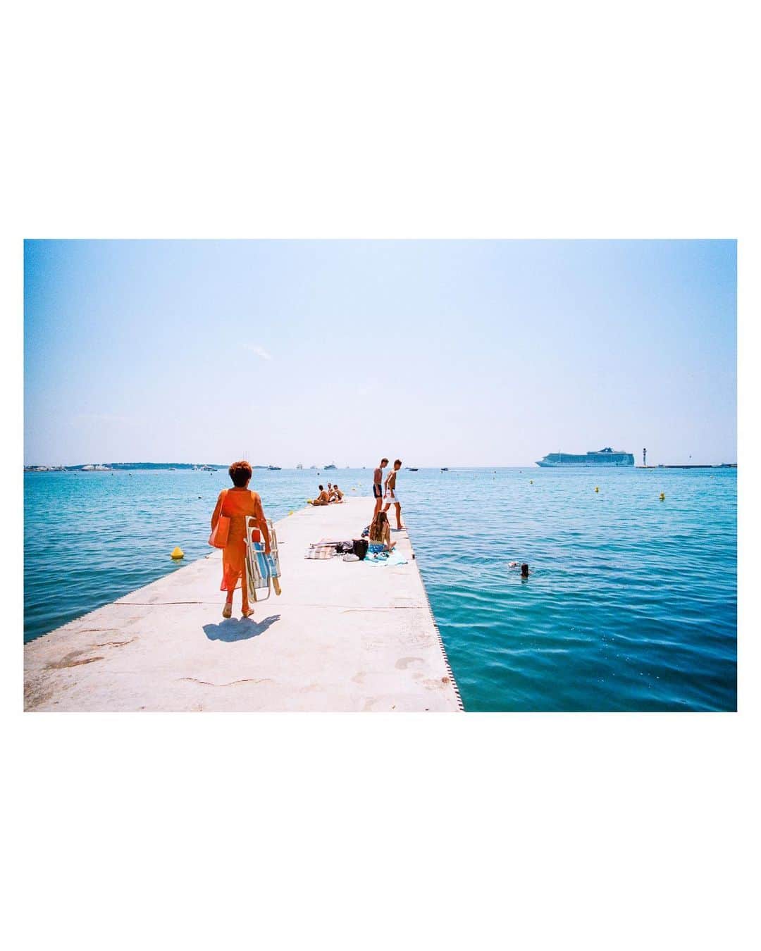 Pete Halvorsenのインスタグラム：「“Dame en Orange”  The lady in orange. While wandering along Boulevard de la Croisette a woman in an orange dress and matching handbag making her way out towards the sea caught my eye. She looked to have stepped out of the 1960s and into 2018. I watched her reach her destination, a small cement jetty where two groups of teenagers were enjoying the sun. There it was a classic Cannes backdrop with cruise ships and blue waters of the French Riviera. I composed the frame...A single moment captured on my Leica, the light frozen in time on Kodak Film...and now minted on the blockchain.」