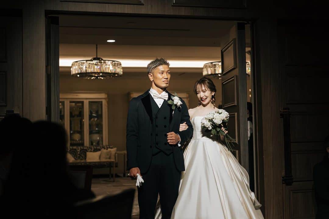 平木愛美のインスタグラム：「wedding 🤍💎🕊💫  入場シーン。  ふたりともさ、、なんとも言えない絶妙な表情！笑  思い出に。載せてみますっ。 #まなみんプレ花嫁   ブーケ、ブートニアのお花は @artificialflower_macherieb  半永久的にずーっと咲き続けるもの。💕🪞💐  wedding dress / antonioriva bridal accessory / a.b.ellie tuxedo / giorgioarmani bow tie / louisvuitton   披露宴会場はストリングス表参道。  挙式を挙げたセントグレース大聖堂と提携されていて、夫のお世話になっている方々など大人数のゲスト様が入る大きな会場でこちらを選びました。  色々と私のこだわりにご対応くださったり、きっと変わったへんてこな夫婦な私たち👱🏿‍♂️👱🏻‍♀️にご対応くださったプランナー様にもとても感謝でした。✨  大きな会場！と、何段もの大きなケーキ！！！は唯一夫のしたかったこだわり部分で⚪️  ストリングスさんのなかでも一番大きい会場"ウエストスイート"  ウッド調だったり大きなグリーンがありつつ、重厚感があり上質な品のあるとても素敵な会場様でした。」