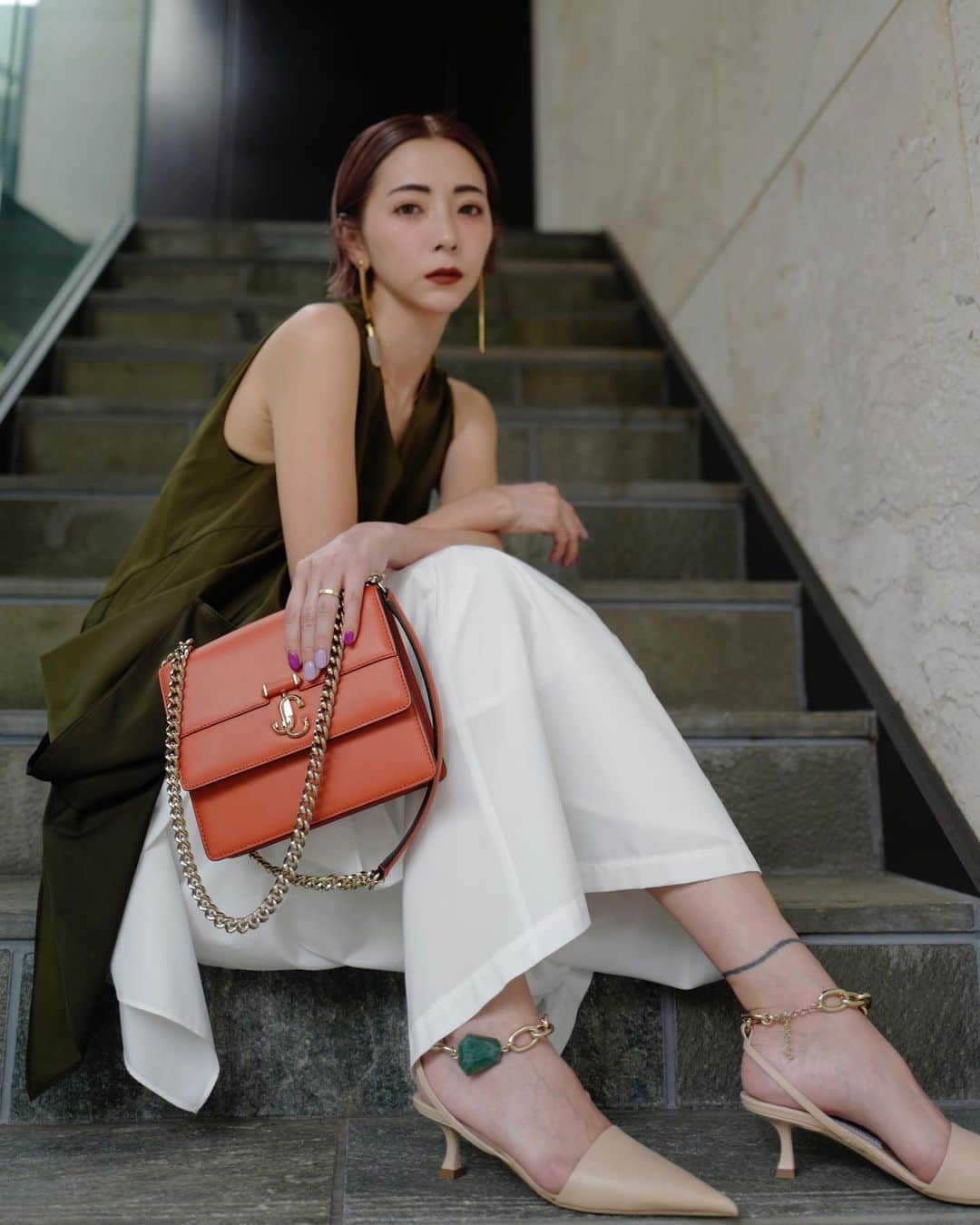 のインスタグラム：「いつものスタイリングも SHOESとBAGで雰囲気が ガラッとドレスアップ😌✨  先日表参道に新しく JIMMY CHOOが移転したので オープニングレセプションにお邪魔しました🥂  JIMMY CHOOのチェーンシリーズが可愛くて一目惚れ💭  ヌーディなミュールに アンクレットチェーンにグリーンのストーン✨  すご〜くタイプだわ  この靴を履きたいなぁと 靴から決めたこの日のスタイリングは  カーキとホワイトでシンプルにSHOESを目立たせつつ  折り紙デザインの立体感でMODEな雰囲気に  オレンジBAGをアクセントに🍊  ちょっとしたパーティやカジュアルな結婚式ならこんな感じで🥂  @jimmychoo   表参道店では オープンを記念して 新作バッグのBON BON STARが5/10まで限定先行販売されてるよ✨  #jimmychoo #jimmychooomotesando #bonbonstar #un3d」