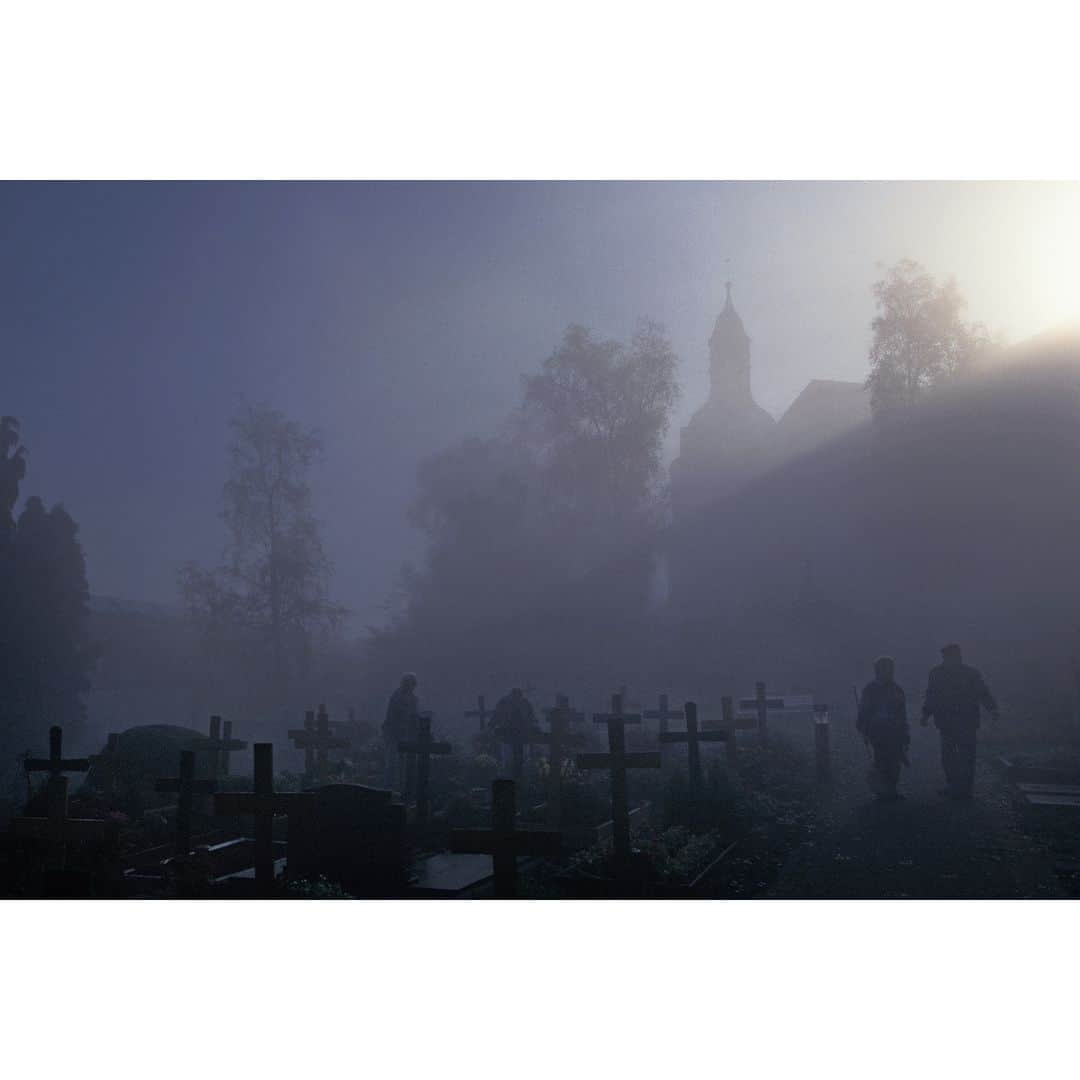 のインスタグラム：「Ethereal and mysterious, fog envelops the old graveyard in Amoeneburg, a village rich in history and tradition in Hesse, Germany. Excavations in the area suggest that the region may have been settled during the New Stone Age.   Amidst the mist, dedicated relatives tend to the graves of their loved ones, their silhouettes barely visible against the church steeple and wooden crosses. Their diligent efforts seem a testament to the enduring bond between the living and the deceased, and the sun struggling to break through the fog, a symbol of hope and renewal in this timeless place.  @thephotosociety @natgeo #Amoeneburg #Hesse #Germany #fog #graveyard」