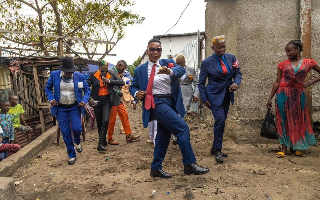 National Geographic Creativeのインスタグラム：「Photo by @yagazieemezi | Walking into the Mikalu neighborhood of Brazzaville, Congo, we were greeted by loud music as members of Mavula Sape approached us in a flurry of fancy dance footwork. Each woman dons her favorite suit for the occasion and calls out nicknames and words of encouragement. The popular spectacle brings neighbors out of their homes to watch the performance. Messani Grace (second from right), the leader of the group, joins in with flourishes of her own. Mavula Sape is part of SAPE (Société des Ambianceurs et des Personnes Élégantes, or Society of Tastemakers and Elegant People), a subculture that can be traced back to the 1920s, when young men, as a form of protest against French-colonial powers, adopted the clothing of their “masters” and created their own unique styles with them. While the men, the sapeurs, have gained international recognition over the years with their dapper and colorful suits, the women (sapeuses) were not as well-known despite having embraced the culture for decades. Women supporting women—whether enjoying a spectacle of expression or engaging in local services provided by women—foster independence of spirit and self. | Global #logistics brand @dhl_global is supporting the SheTrades Program, amplifying cultural and social movements across the globe and encouraging female entrepreneurs to play a bigger role in society and the economy.」