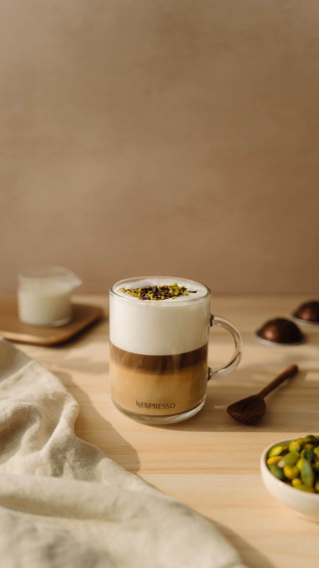 Nespressoのインスタグラム：「Because what’s life without a little something sweet?   Celebrate this Easter with our latest Nespresso recipe: a creamy base of rich chocolate, topped with Nespresso Barista Milk Creations coffee, velvety frothed milk, and crunchy pistachios. ☕️✨  ☕️ Here’s how to make it:  1-Pour 10 ml of salted pistachio syrup and 5 ml of dark chocolate sauce into a Vertuo long cup. 2-Extract 40 ml of Bianco Piccolo directly into the cup and pour over 110 ml of hot milk foam. 3-Top with crunchy pistachios and shaved dark chocolate to finish. 😋  #Nespresso #NespressoVertuo #NespressoCreativeCups #Easter」