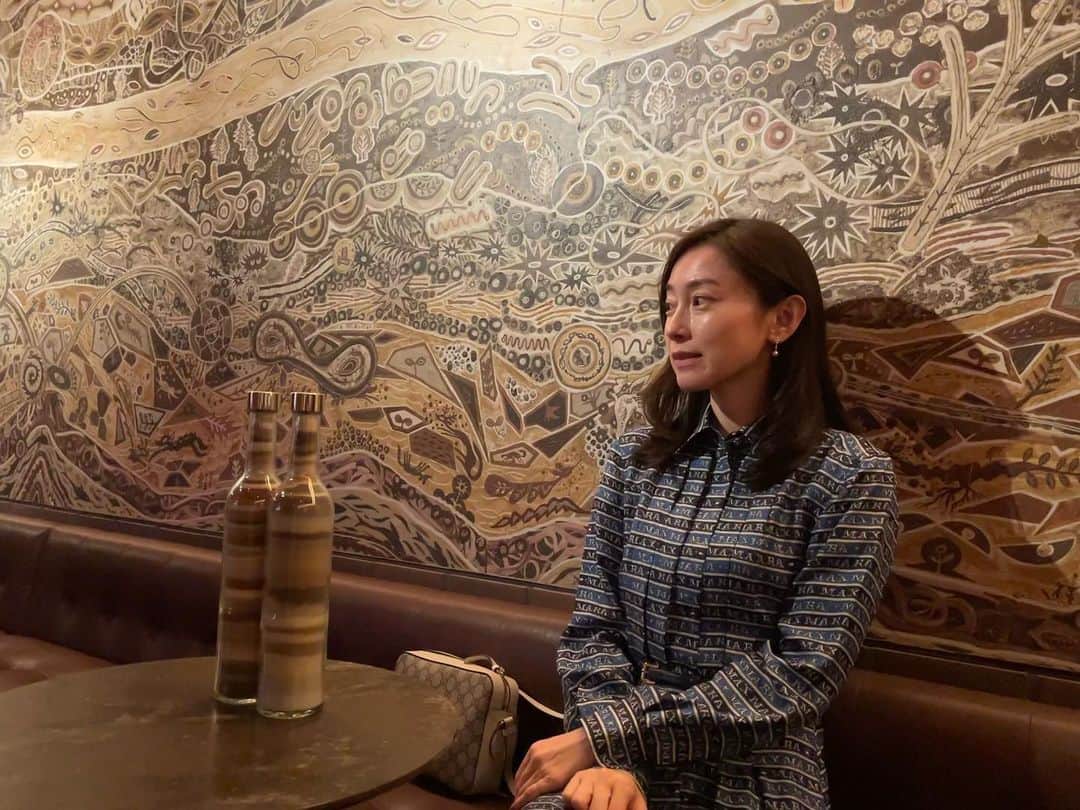 小橋めぐみのインスタグラム：「東急歌舞伎町タワー 地下2階のバーラウンジの壁面を飾るのは 淺井裕介さんの 大地のこだま という作品。 こちらは、なんと泥絵！  淺井さんが集めてきた日本各地の土に加えて、この施設の建設現場や新宿駅の神社や公園などから採取した土を用いて、音楽と地層、水脈をテーマに、生命が育まれ、リズムを持って躍動するイメージが描き出されています。  私の前にあるボトルは、採取された土の層。 土にも、こんなに様々な色があるのかと驚きました。  泥絵というものを初めて見たのですが、 温もりと懐かしさを感じ、 ここでお酒を飲んだら寝てしまいそうなほど、落ち着きました💤  #東急歌舞伎町タワー #淺井祐介 #写真3枚目は淺井祐介さん #art #新宿バー」