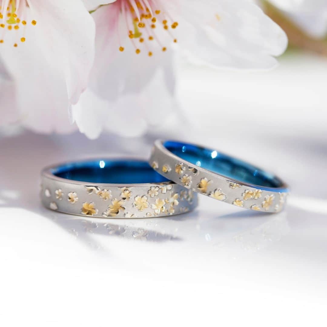 SORA ≪SORA表参道の公式アカウント≫のインスタグラム：「#結婚指輪SORA 【KASUMISAKURA-霞桜-】 青く澄み渡る空に散りばめられた愛らしい桜の花々🌸 そんな春の情景を指輪にしました。  新緑たけなわの頃、木全体にまばらに 薄ピンク色の花を咲かせる #霞桜 は、 遠くから眺めると霧のように見えることが 名前の由来です。  繊細な立体表現が魅力のデザインは、 クリエイターの高い彫金技術によって叶いました。  まずは原板に一打一打、桜の花びらを刻み、 そこに指輪になるプラチナの板を高圧で押し当てて、 桜の模様を写しとりました。  花びらの部分にほんのりゴールドの彩りを加え、 指輪の内側には発色ができる ジルコニウムの金属を用いることで、 霞桜の世界観をさらに際立たせます。  クリエイターの愛情と時間をかけて仕上げた指輪を ぜひ店頭でお手に取ってご覧ください。  ◤霞桜 取扱店◢  ・SORA表参道本店 ・SORA札幌店  - - - - - - - - - - - - - - - - - - - -   🟩LINEでもデザインのご相談が可能です >>>「SORA」と検索！  公式アカウントをお友だち登録して メッセージを送ってください  SORA表参道本店のデザイナーがご返信します💁‍♀️  - - - - - - - - - - - - - - - - - - - -   SORA公式サイトや店舗情報は アカウントTOPのURLからcheck * >>> @sora_omotesando  ぜひハッシュタグをつけて SORAの写真を投稿してください♪ >>> #結婚指輪SORA  デザイナー、クリエイターが皆さんの投稿を拝見し 毎日パワーをいただいています🌿  - - - - - - - - - - - - - - - - - - - -   #結婚指輪 #結婚指輪探し #結婚指輪オーダーメイド #weddingring #ペアリング #金属アレルギー対応 #プレ花嫁 #2023wedding」