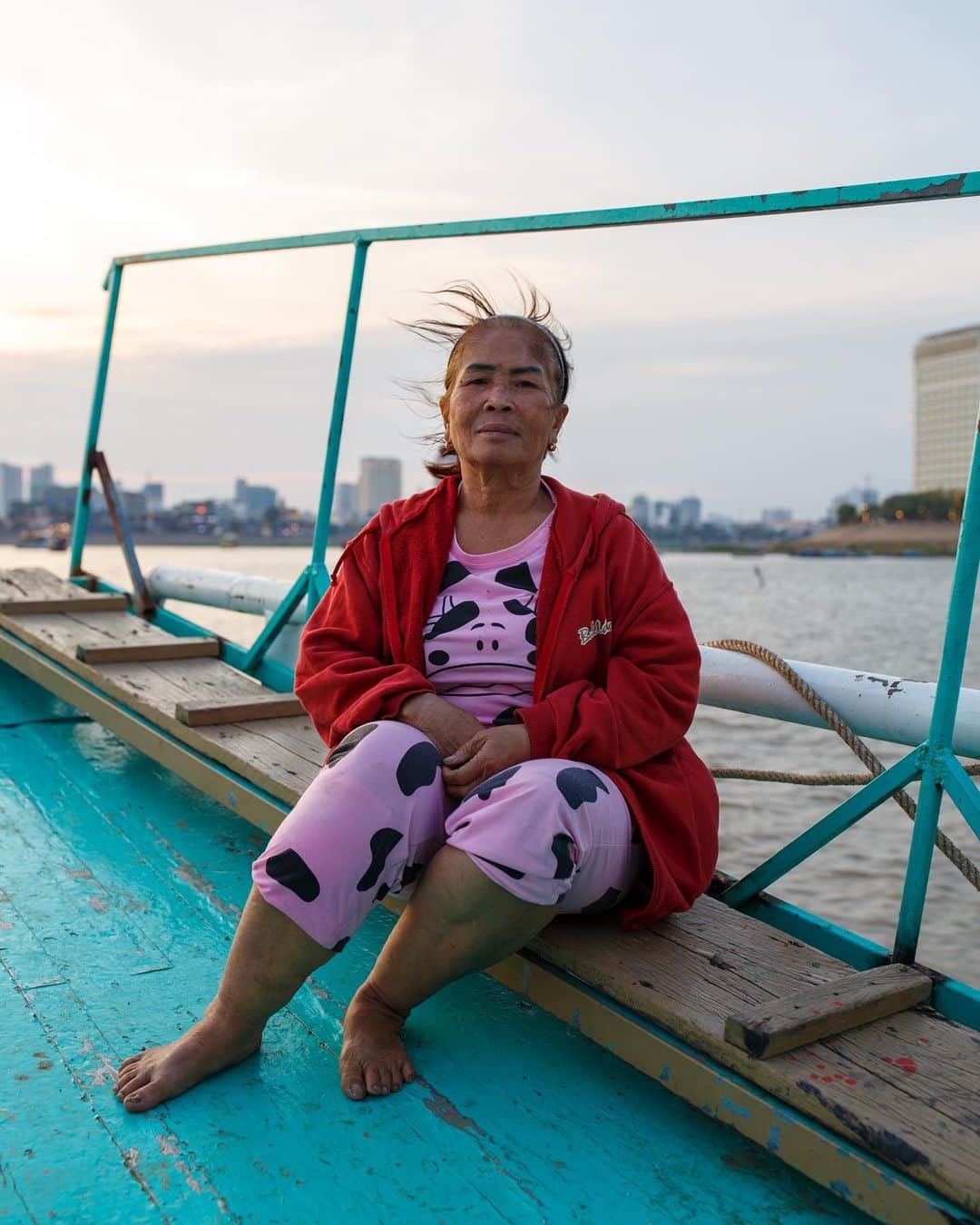 Shunsuke Miyatakeのインスタグラム：「Vice Captain of a cruise boat /  There are two major rivers flowing through Phnom Penh. The Tonle Sap River and the Mekong River. In the evening, many cruise boats carry passengers and move slowly along the rivers.  The time spent on the boat watching the sunset over Phnom Penh is exceptional. Some people are surprised at the changing cityscape, while others worry about the people who continue to live on the water in Areiksart.  The vice captain likes to live with her family on the boat.  Even though the cityscape has changed, some people continue to offer cruise boats and continue to enrich their customers' lives as usual.  #phnompenhphotographycollective」