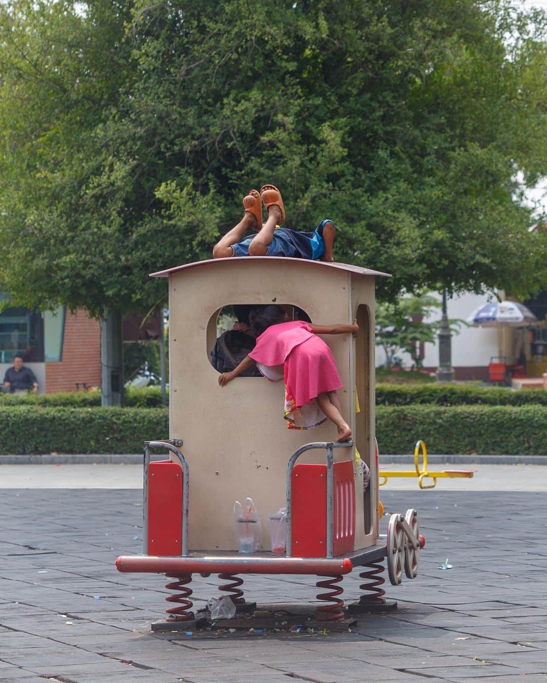Shunsuke Miyatakeのインスタグラム：「Curiosity /  Several children are playing in a park. A large child hides in one of the train-shaped boxes. The smaller children peek inside from above and behind.  They lie on the platform or climb up on their bare feet. They don't care what they look like. They just want to know what is going on inside and who is there.  Our views tend to become more and more fixed as we get older, especially as we gain more experience and knowledge.  If we look at things from different angles, from above and behind, we can see what is going on inside from multiple perspectives.  The big kid in the box was drinking juice behind the little ones 🥤  #phnompenhphotographycollective」