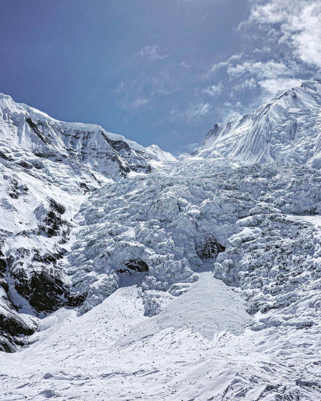 石川直樹さんのインスタグラム写真 - (石川直樹Instagram)「#Annapurna from the crampon point, #Nepal. 今日はクランポンポイントまで体慣らし。写真は、4500m地点から眺めたアンナプルナI峰。2枚目の写真が、山の左側にある懸垂氷河。この懸垂氷河の左を登って右に回り込み、右上方にトラバース、最後にフレンチクーロワールを400m登った先が頂上だという。 岩波少年文庫（近藤等訳）によれば、#アンナプルナ はネパール語で「収穫の女神」。地図を見ていると、アンナプルナ山群が無数の小さな川の水源になっていることがわかる。この氷河から流れ出た水が周囲の村を潤し、人々に恵みをもたらしてきたのは間違いない。 しかし、一方でこの山は「キラーマウンテン」というありがたくないニックネームも持つ。それはルート上で雪崩が多すぎて、これまで多くの遭難を引き起こしてきたからだ。昔、ミンマに14の山でどれが一番難しいと思うか、と尋ねたところ、即答でアンナプルナだった。 雪崩のリスクの少ない迂回ルートが近年になって新しく拓かれたことで、2021年には記録に残る大量の登頂者もだした。だが、それでも不安は残る。アンナプルナとは、そういう山だ。 . #Himalayas#Glacier」3月24日 18時06分 - straightree8848