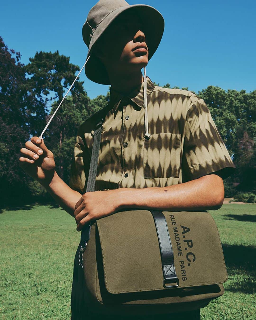 アーペーセーのインスタグラム：「@issouuuuuuuuuuuuuu wears the Sense satchel, the Ross short-sleeve shirt with tie-dyed print and the Rachel bucket hat.  The Sense satchel in khaki is only available in the US and in selected stores.   Creative direction & Styling: @suzannekoller Photography: @samrocksamrock  #APCParis #APCSS23」
