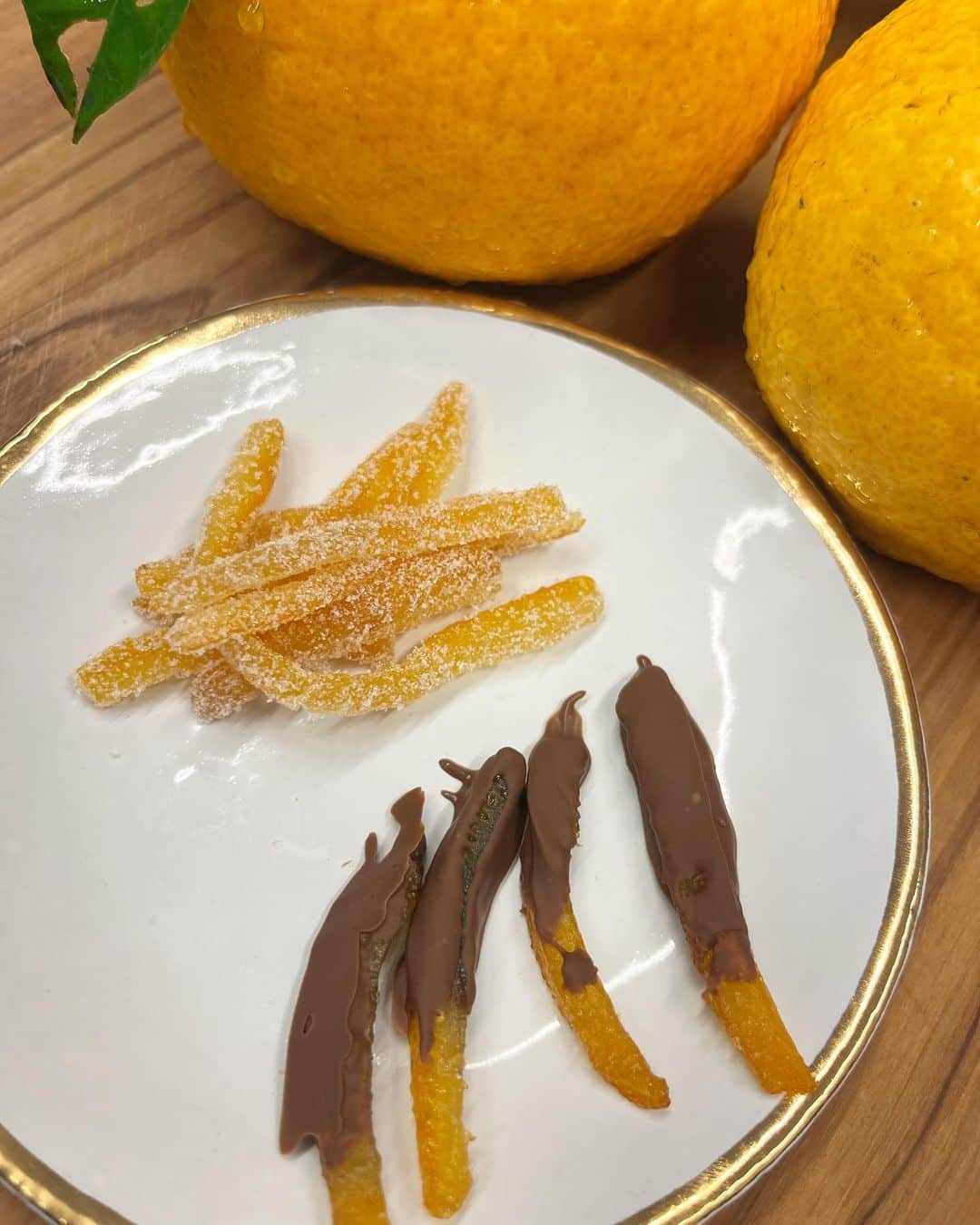 のインスタグラム：「今朝のお庭柑橘でオレンジピールを作りました。ジューシータイプ。  「オレンジピール食べる？」と聞いたら、「チョコがかかってないからいらなーい」by 宇宙人。 笑😊という事で、作った2種。 ガーナくんがあったから作れました。  私のオレンジピールは割と簡単です！ 内側のワタをスプーンで取り、カットします。鍋でグツグツしてお湯を捨てるを２回繰り返します。 舌が痺れたくない方は３回😊 水を切って糖類をお好きな分入れます。（しっかり甘い方がおいしいです）糖類が溶けたら焦がさないように混ぜながら火にかけます。 水分が飛んだら、クッキングシートの上に並べて乾かします。 しっとりが好きな方はこのまま乾かし、硬いのが好きな方はオーブンで5分から10分。  冷めたら、ビニール袋にオレンジピールと糖類をプラスしたら出来上がりです。  私はてんさい糖の白いのを使いました。黒糖でもおいしいです。」