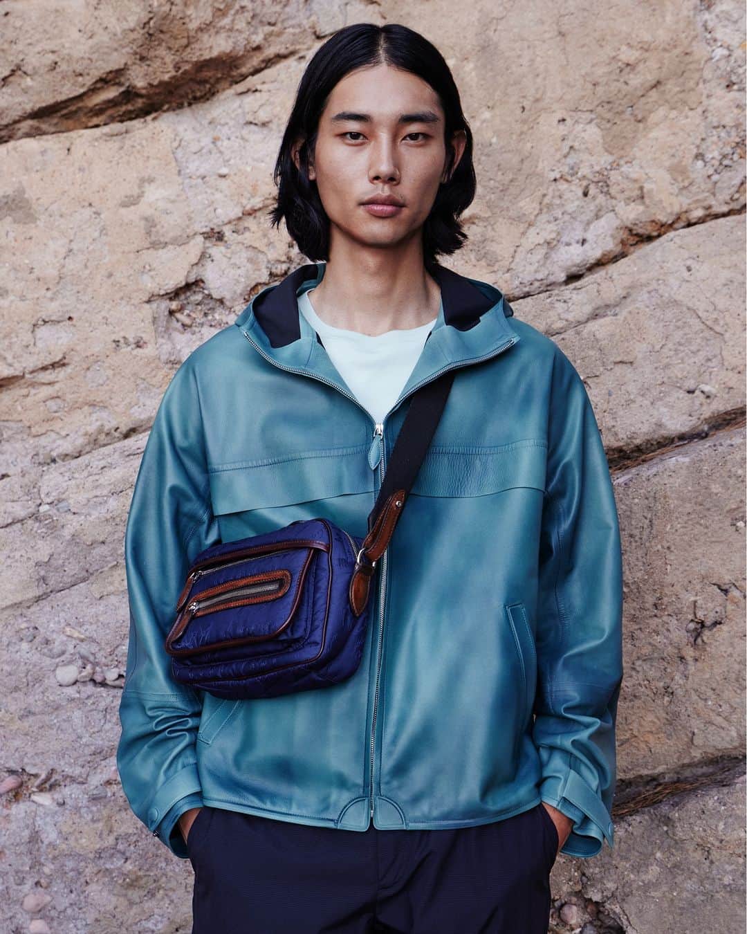 ベルルッティのインスタグラム：「- THE SILHOUETTE BY #BERLUTI -   Made of soft, extra fine leather, a waterproof windbreaker becomes an unexpected hero piece for Summer 2023. Now available in Dark Dusty Blue, a splendid color which matches perfectly with our Nylon Scritto Messenger Shoulder Bag. A combination that makes for an airy and effortlessly chic silhouette.   Now available online and in-store.  Styling by @virginiebenarroch  Photography 1 by @anthonyseklaoui  Photography 2 by @philengelhardt   #BERLUTIDRIVE」