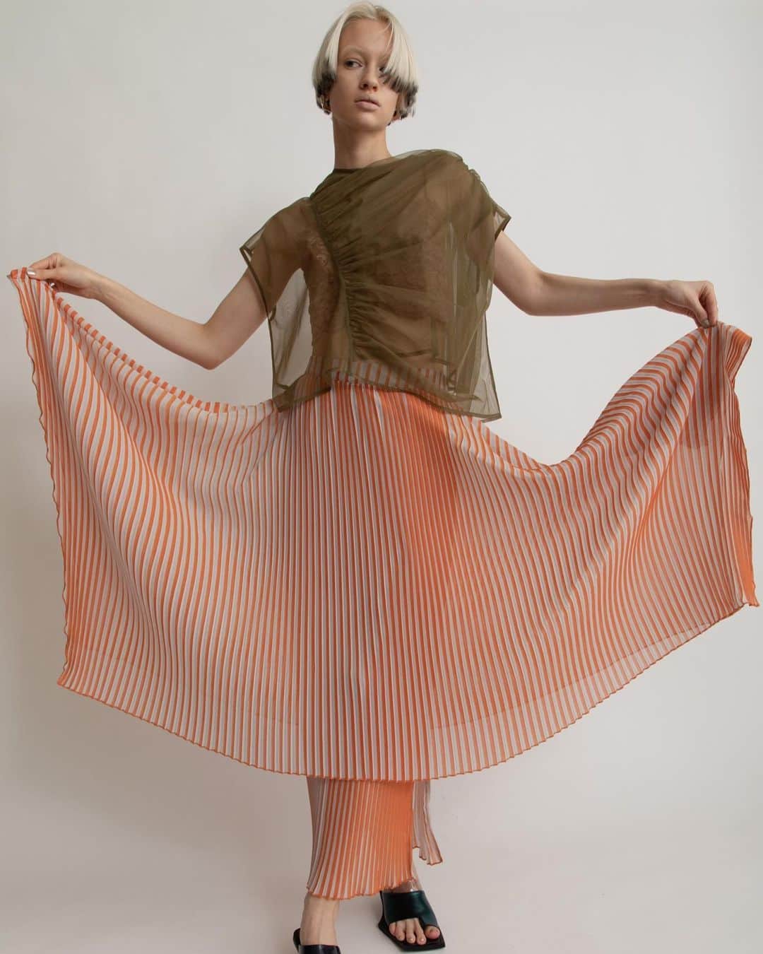 AULA AILAのインスタグラム：「【2023 HIGH SUMMER COLLECTION】  TULLE GATHER TOPS SET COLOR KHAKI×OFF SIZE 0 ¥16,500  ナイロンソフトチュールのトップスと、スリーブレスのカットソーがセットになったアイテム。 チュール部分は、ふんわりと体を包み込むように、アシンメトリーに寄せたギャザーを重ねて、透け感がありながら立体感のある表情に。 単品でワンピースやお手持ちのトップスに重ねて着まわすのもおすすめです。  STRIPE PRINT PLEATS SKIRT COLOR ORANGE×LT.GRAY SIZE 0/1 ¥23,100  細いプリーツとストライププリントの加工を施したオリジナル生地をレイヤードしたスカートです。  内側スカートは左裾にスリットが開いたタイトラインで、表スカートは広げると長方形になるデザイン。 プリーツとストライプの縦柄効果が、造形的でシャープな印象のスカート。  ✔️AULA AILA OFFICIAL WEB STOREにて HIGH SUMMER COLLECTIONアイテム展開中！」