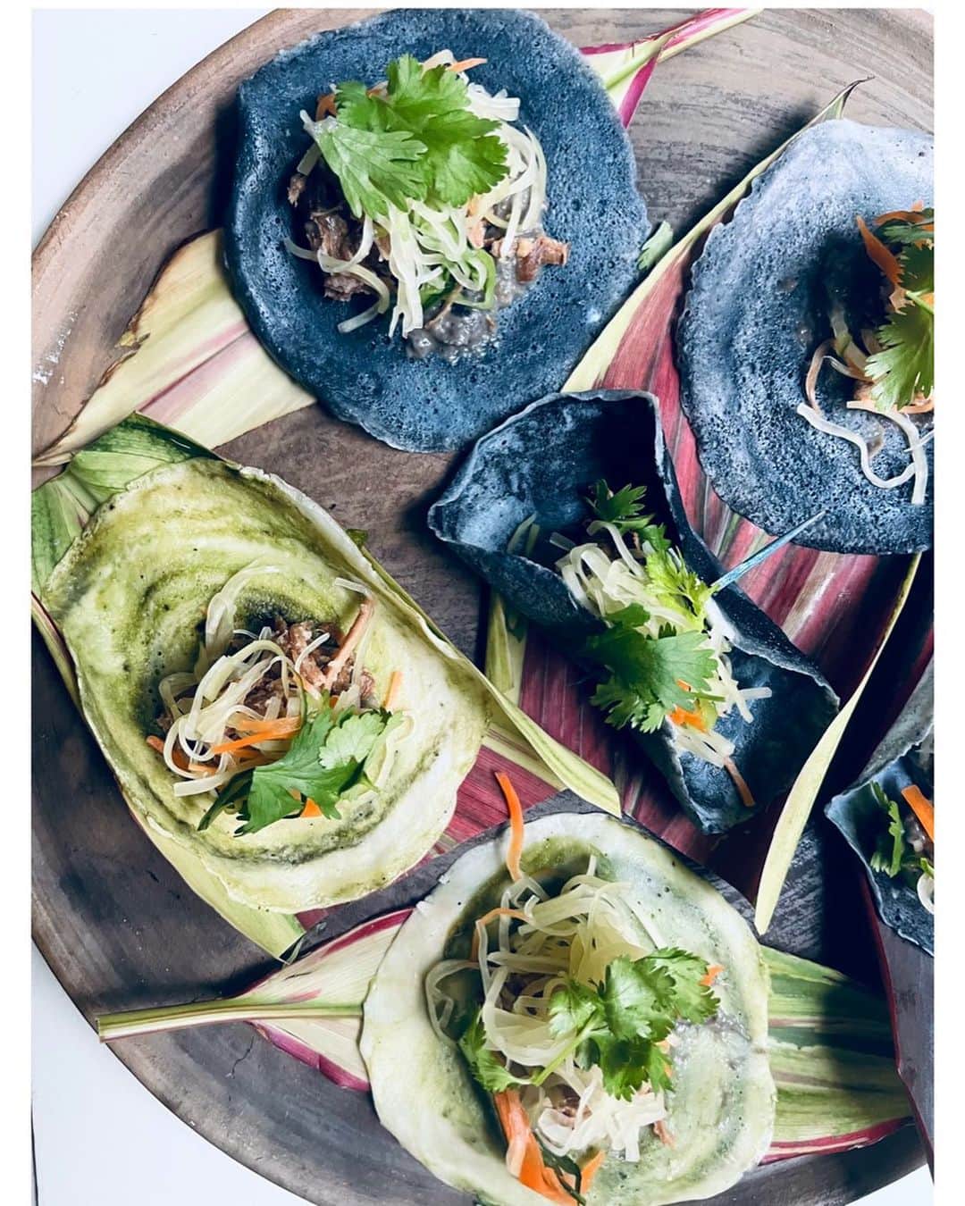 journaleatripのインスタグラム：「Japanese tacos mud dyeing  敬愛してやまない3人が 合わさった展示 "HIRAKI project 泥中の布"  作らせて頂いたのは 奄美の食材を送って頂き米粉と炭、緑葉の生地に月桃茶と黒糖、黒糖焼酎煮た豚肉にパパイヤと島味噌ペーストを合わせた奄美タコス？でした。黒糖バナナケーキナッツなど。  「残すべきものはなにか?変わっていくことはなにか?」 1300年続く大島紡ぎの未来はこの3人の顔をみていると灯火が消えいりそうな状況の中とはいえ沢山の来場した方々とともにヒカリの筋がみえました。 有難うございました。  そしてみなさま是非足をお運びくださいませ。  .......................  HIRAKI project 泥中の布 大島紬は、1300 年の歴史を歩んできました。 明治 10 年頃、車輪梅 ( テーチ木 ) で下染めし、泥田に浸ける染色技法の「泥染め」が 主流となります。 明治 40 年には「締機 ( しめばた )」が開発されたことで、 世界でも類を見ないほど、緻密な絣柄の表現が可能となります。 その後、大島紬は奄美の一大産業として、飛躍的に発展しますが、 現在の生産反数はピーク時のわずか 1%ほど、年間 3,000 反以下。 生産に関わる多くの職人も高齢化していることが現実となっています。 「残すべきものはなにか?変わっていくことはなにか?」 1300 年のなかで新しい技術を取り入れながら、変化を遂げてきた大島紬だからこそ、 新たな変化にも順応し、取り入れていくことで、 この伝統を未来に繋いでいくことはできるのではないでしょうか。 今回、泥染の下染に主として用いられていた、車輪梅 ( テーチ木 ) の手法を見直し、 車輪梅に加え、インド藍、蘇芳、福木、柳の5種を下染を施し、 新たな泥染の可能性を試みたことにより、今まで見たことのない 泥染の色と出会うことができました。 また織組織も一反毎に変えており、組織織特有の色の見え方、生地の風合いを表現 しています。 この変化の一端が大島紬の表情をより増やしていき、 過去から現在、 そして未来へと新たな可能性を探る気付きになればと思っています。  金井 志人(染色) 柳晋哉(織 ) 泉二啓太(企」