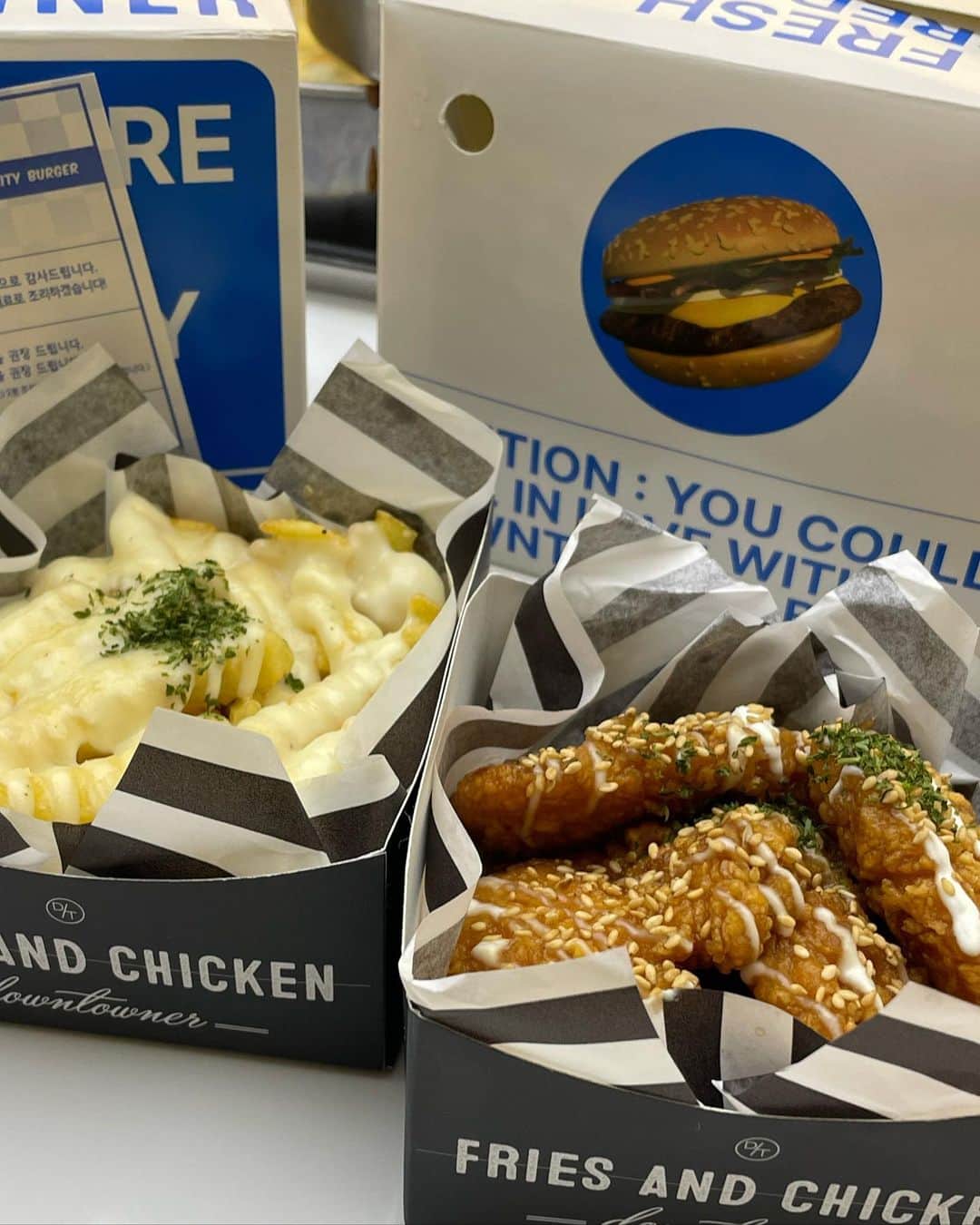のインスタグラム：「@downtowner.official 🍔💙  韓国でケーキの仕込みしてて、 普段仕込み中あんまり休憩しないって伝えたら、 「ダメダメダメ✋」ってハンバーガー買ってきてくれた涙  ハンバーガー屋さんだけど、 このポテトとチキンが美味しくて美味しくて是非これを食べに行って欲しい！笑  ポテトには甘いソース チキンは辛くないけど、タレチキンで永遠食べられる味だった...  私ボリューミーなハンバーガー普段好んで食べないから（食べにくい食べ物が面倒な人） こゆ系ハンバーガー大好きなおじおじがとっても嬉しそうでした🤫💙  #downtowner #downtownerburger  #다운타우너 #1日1こうこりあさんぽ」