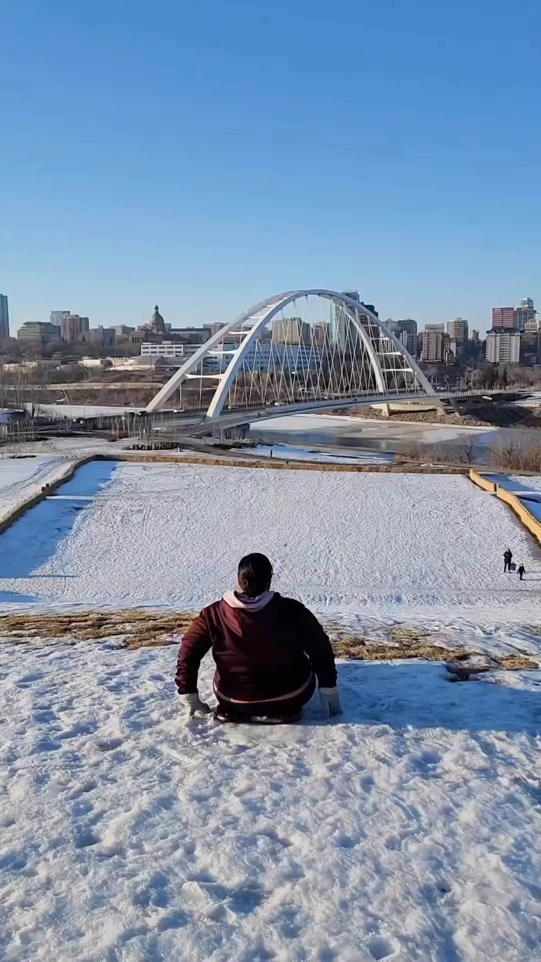 のインスタグラム：「You always remember the last toboggan run of the season! 🛷☀️   📷: @yegventures  📍: @exploreedmonton, @travelalberta   #ExploreEdmonton #ExploreAlberta   [Video description: A person in a light jacket sleds down a hill with a light layer of snow, spring grass can be seen on the edge of the snow. At the end of the hill is a view of a large white arched bridge for vehicles.]」