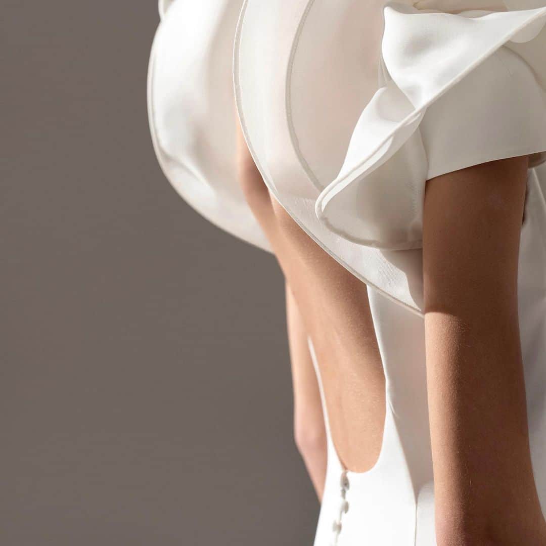 ステファンローランのインスタグラム：「EPURE Inspired by the designer's haute couture creations, these 10 silhouettes are already available in the Parisian showroom.   TOUTE UNE VIE Long dress in white crepe embellished with orchid sculptures of gazar on the shoulders.  The back is elegantly revealed and bares a delicate line of buttons covered in the same crepe as the dress.  #StephaneRolland #Bridal #Wedding」