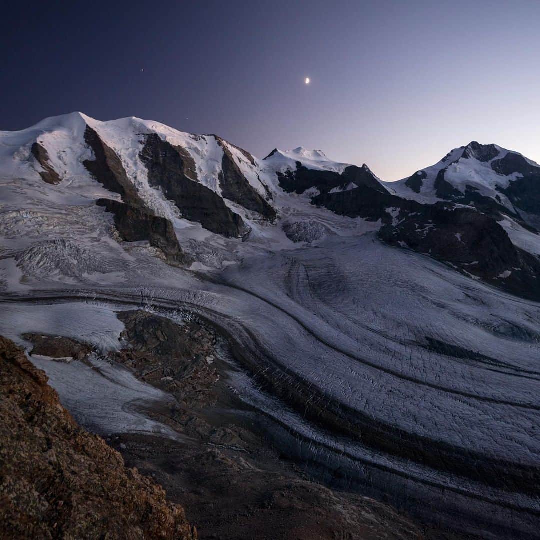 クリス・バーカードのインスタグラム：「Once the sun dips behind the jagged spines of the Swiss Alps, the wind dies down and all you hear is the occasional croak of the glacier and a distant rush of melting water beginning a long journey to the valleys below… your eyes tracing ridge after ridge until they fade into the soft blue horizon. The mountains have a special way of inspiring a sense of calm and awe simultaneously… something that draws you back.   Shot in 2019 on the @sonyalpha A7RIV, FE 16-35mm f/2.8 GM  ISO: 400 Aperture: 2.8 Shutter: 1/3   #SonyArtisan #SonyAlpha #SonyPartner」