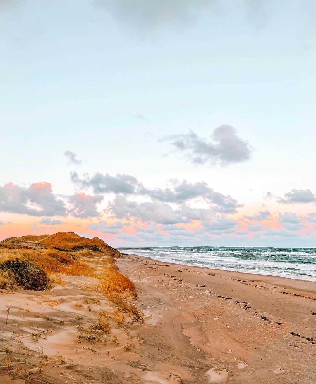 Explore Canadaのインスタグラム：「Days like this remind us that summer is on the way ☀️  Are you feeling any warm weather where you are?  📷: @peicameraroll  📍: @tourismpei   #ExplorePEI  [Image description: Sand dunes next to a long sandy beach. Small waves wash ashore. The sky is pale blue and orange.]」