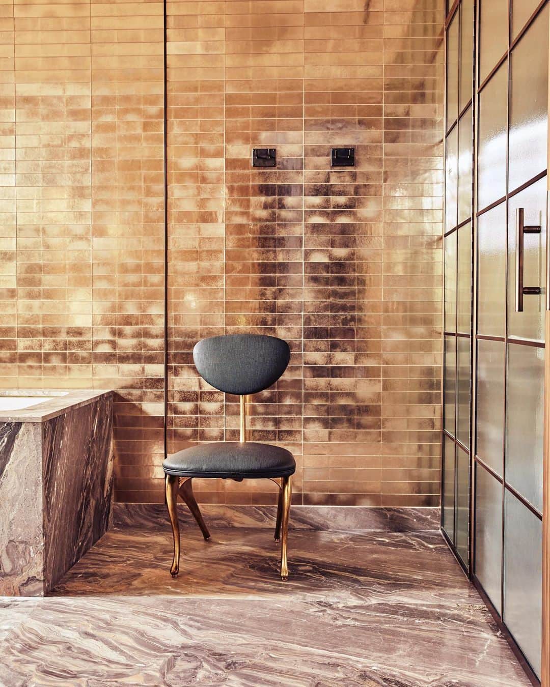 ケリーウェアスラーのインスタグラム：「NATURAL OPULENCE. In this private residence, the master bath is an ode to natural materials in their most glamorous incarnations. Painted brass divided light doors frame ribbed glass, walls are clad in luminescent glass tiles, and vintage smoked glass sconces, etched with a wave motif, illuminate the space. XK」