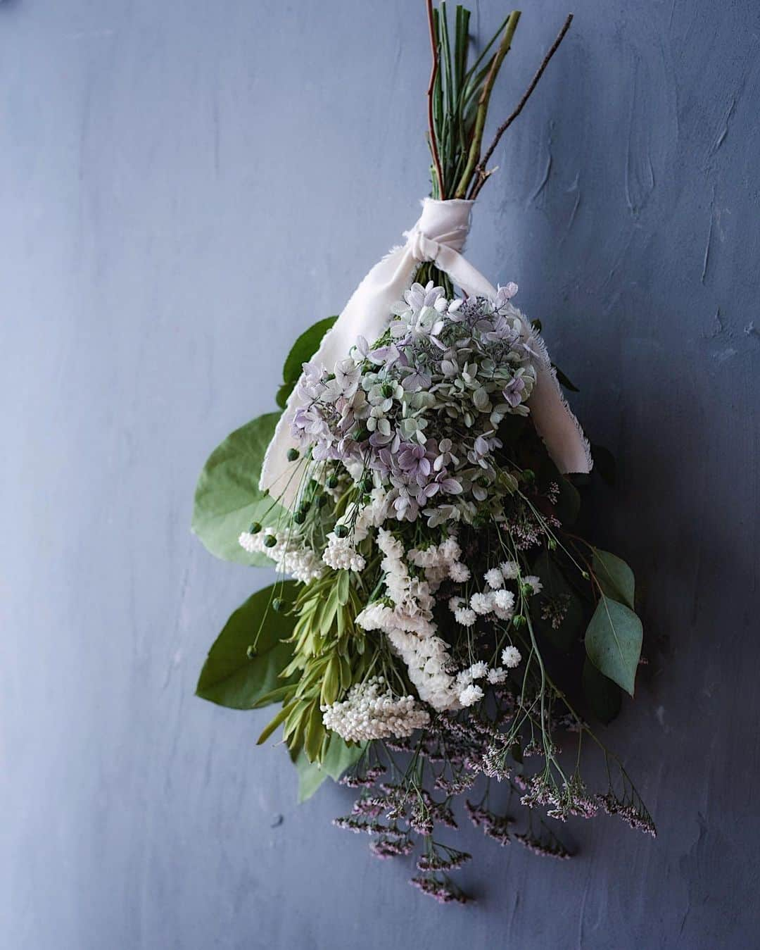 増田由希子さんのインスタグラム写真 - (増田由希子Instagram)「Mother's Day Bouquets (pre-order only) #bouquet #swag #driedflowers #hydrangea   < 母の日ギフト・ スワッグ販売のお知らせ >     「紫陽花と亜麻の実のスワッグ」   手毬のような紫陽花に小花とグリーンを添え、亜麻の実を散りばめました。  亜麻の花言葉は「感謝」。  「いつもありがとう」の想いを込めて、 母の日に、大切な方への贈り物に。  【予約販売期間】 4月27日(木)10時〜5月1日(月) 【お届け日】 5/12(金)、5/13(土)、5/14(日) 但し、遠方（北海道、沖縄）の場合、14日(日)までにお届けできない可能性がございます。 【取扱店】  kanon（山梨） @oyatsu_utatane  プロフィールリンクよりWeb shopにアクセスしてください。 【価格】7,200円 (税別) ※価格には、メッセージカード付きラッピング代が含まれています。 ※別途、送料がかかります。 【サイズ】全長約55cm〜60cm 幅約20cm 高さ約13cm   🌿スワッグには、プリザーブドとドライフラワーを使用しておりますので、長く飾って頂くことができます。  🌿ライスフラワーは、白かピンクどちらかが入ります。(色の指定不可)  🌿ギフト包装について イラストレーター みやしたゆみさんデザインの包装紙とThank youカードを添えてお届けします（今回kanonさんに特別にご用意いただきました）   ※自然素材を使用しております為、花材の一部が変更となる場合がございます。」4月26日 18時09分 - nonihana_