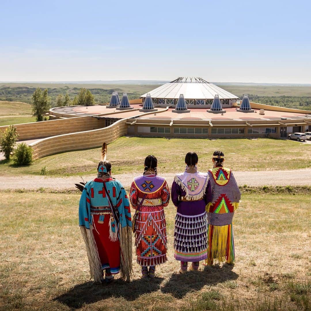 Explore Canadaのインスタグラム：「When you visit an Indigenous tourism business, you’ll experience culture and build meaningful connections to the past, present and future. You’ll hear stories, songs and legends that have been passed down through countless generations.   For many Indigenous communities across Canada, Traditional Knowledge and storytelling are vital for preserving culture, language, ways of being, and educating future generations while providing necessary connections to their ancestors. Whether they are creation stories, medicine teachings, or historical accounts of lived experiences, they have been shared for thousands of years, many without ever being transcribed.  These traditions and stories are shared within communities by Elders. But across the country there are also many cultural centres open to the public that ensure Traditional Knowledge is accessible to everyone. Whether it be multi-sensory, full immersion cultural centers or archival museums you can experience the history of living, breathing cultures and gain a deeper understanding of the lands you are on.  Visit @destinationindigenous’s link in bio for a list of culture centres you can experience across the country.   📍: @blackfootcrossing, @indigenous.tourism.alberta  📍: @destinationcarcross  📍: @ojibweculturalfoundation, @indigenoustourismontario   📷: @travelalberta, Archbould Photography, Sebastien Desnoyers  #DestinationIndigenous #TheOriginalOriginal  [Image descriptions: 1. Four people face away from the camera towards the Blackfoot Crossing Historical Park’s main building and the Alberta plains beyond it. Each person wears Blackfoot regalia. 2. Two people walk along a boardwalk at Carcross in front of a building painted with a large black, red and teal mural of Indigenous design. 3. A collection of meaningful objects sit atop a stone mantel: a wooden bowl and feather, braided sweetgrass, small baskets, matches.]」