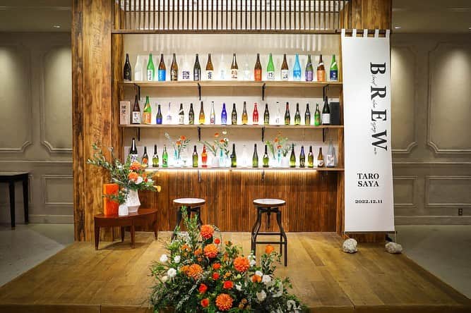 のインスタグラム：「． テーマは「BREW」 Blend・Relax・Enjoy・Waveの頭文字を取っています。大好きな人と混ざり合って最高に楽しくリラックスしワクワク感のある一日に。その想いをおふたりが大好きな日本酒を使って表現しています。メイン席はカウンターと日本酒の瓶を飾った棚で装飾し、日本酒バーのように仕立てました。  #tg花嫁 #wedding #ウェディング #結婚式 #プレ花嫁 #卒花 #卒花嫁レポ #TRUNKBYSHOTOGALLERY #デコレーション #日本酒 #リラックス」