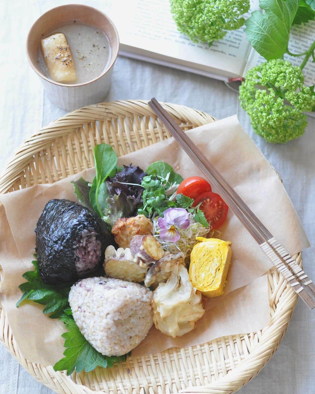 masayoのインスタグラム：「2023.5.1  +lunch ・ @otomarche で買ってきた @hitomi___hashimoto さんの テトラむすびとスープで おうちランチ♪ ・ 4月はやさいがやさしいお弁当を いただいたのですが 今回はこの形がかわいい テトラむすびが食べたくって^^ ・ 4種類あって 黒米に小梅が入って海苔で巻いたのと 玄米と雑穀にふきと新生姜のを 選んできました。 スープは新玉ねぎのすりながし。 スープはスープジャーを持参すると 少し多めに入れてもらえて◎ もちろん！持っていきましたよ〜！ どちらも美味しい〜。 ・ あとは、お弁当の残りに サラダを添えてワンプレート。 ・ お花は @hi_la_la さんで。 ・」