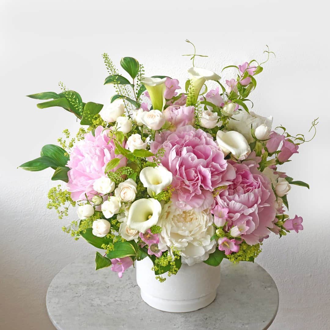 AOYAMA_HANAMOさんのインスタグラム写真 - (AOYAMA_HANAMOInstagram)「大輪の芍薬と、旬の花々の穏やかなハーモニー。 ・ 淡いピンクと白の大輪の芍薬（ピオニー）に、白いスプレーバラやカラー、ピンクのカンパニュラを合わせたアレンジメント。細やかなリーフのあしらいがナチュラルさを加え、エレガントな仕上がりです。 ・ 芍薬は、その華やかな姿から「立てば芍薬、座れば牡丹、歩く姿は百合の花」という言葉にも登場する、日本を代表する美しい花の一つ。 花色はピンク・赤・白など、咲き方は翁咲き・バラ咲き・手毬咲きなどさまざまです。 この時期ならではの、豊富な品種の芍薬をお楽しみください。 ・ 商品名：芍薬のアレンジメント＜シャルール＞ - - - #aoyamahanamo #青山花茂 #お花のある生活 #花が好きな人と繋がりたい #花を贈ろう #花のある暮らし #花のあるくらし #花のある日常 #癒しの花 #季節の花 #旬の花 #花とおうち時間 #花贈り#フラワーギフト #花の贈り物 #アレンジメント #芍薬アレンジメント #ピオニーアレンジメント#芍薬 #シャクヤク #ピオニー #かぐや姫 #白雪姫 #カラー #バラ #スプレーバラ #カンパニュラ  #初夏の花」5月4日 18時00分 - aoyama_hanamo